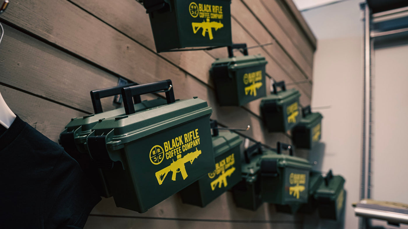 Green boxes labeled Black Rifle Coffee Company with yellow logos and rifle graphics are mounted on a wooden wall in a retail display.