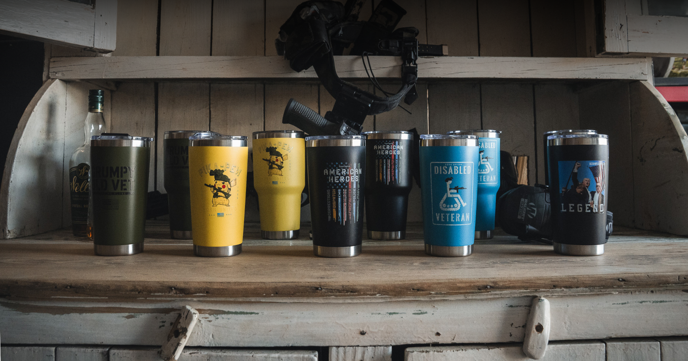 Eight travel mugs with various designs and military-themed texts are displayed on a rustic wooden shelf, with a bottle and tactical gear in the background.
