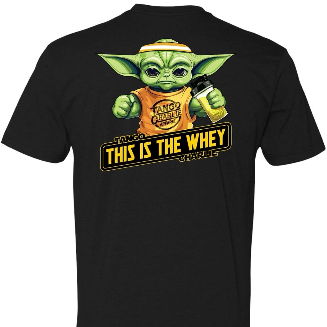 A black t-shirt by Tango Charlie Apparel called The Whey displays a large-eared, green-skinned character holding a bottle. It features yellow text: Tango Charlie Apparel and This is the Whey, highlighting whey proteins muscle-building power.