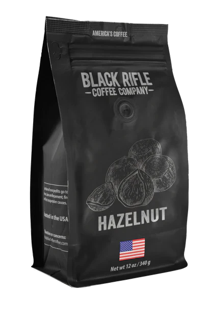This 12 oz bag of Hazelnut Coffee Roast - Ground from Black Rifle Coffee offers a bold flavor. The sleek black package features hazelnuts and an American flag, blending robust taste with patriotic flair.