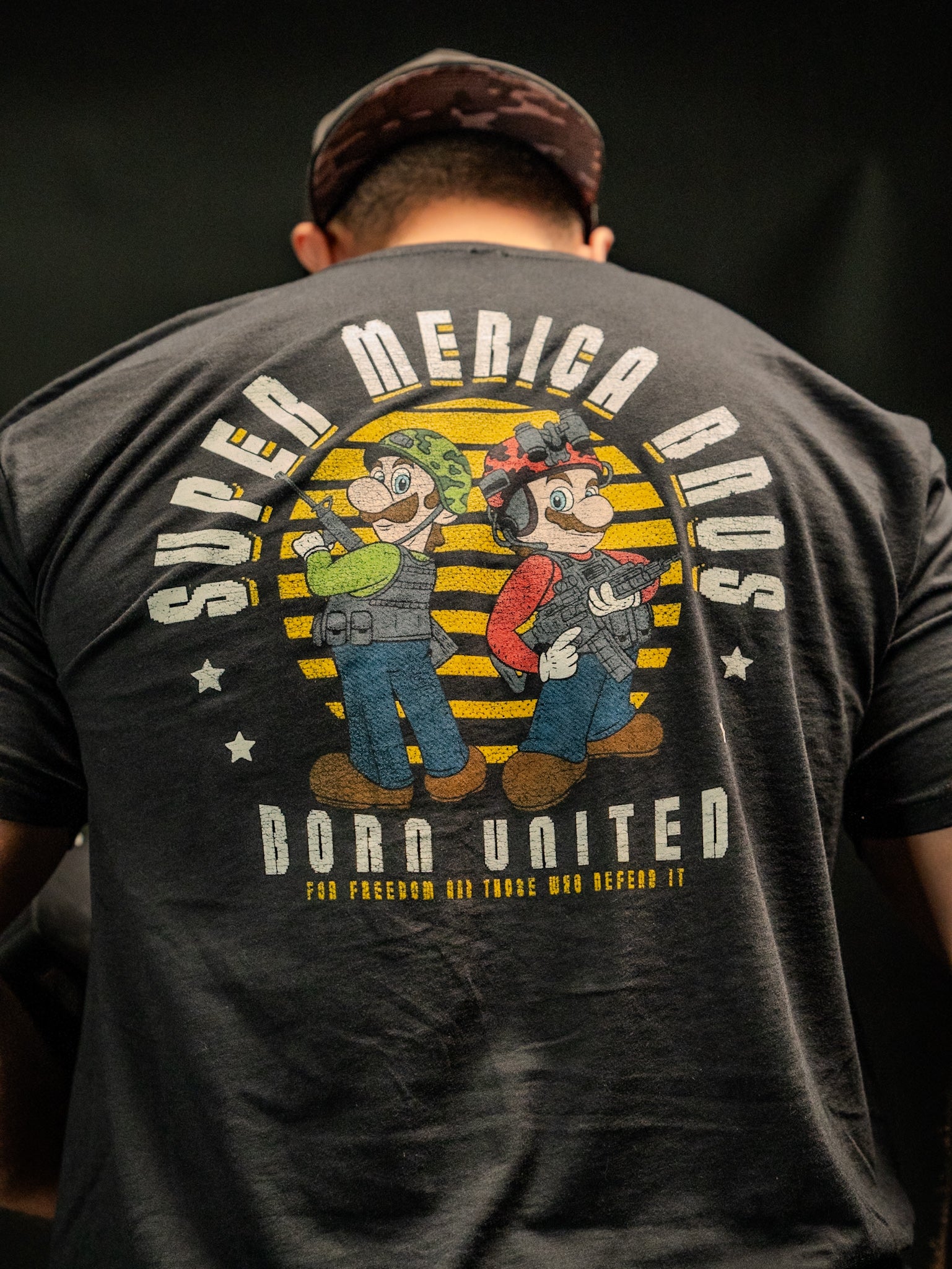 A man wears a Born United Private Label tee featuring a vivid graphic of two cartoon-like plumbers. Super Merica Bros and Born United are on the back, adding an all-American flair to your wardrobe.
