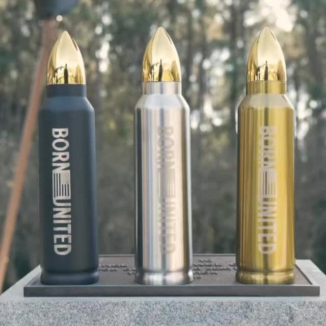 Three Bullet Thermos bottles from Born United Private Label, featuring a gold cap and Born United text, appear in black, silver, and gold on a stone pedestal outdoors. The scene creates a serene Five Sip experience against a blurred forest backdrop.