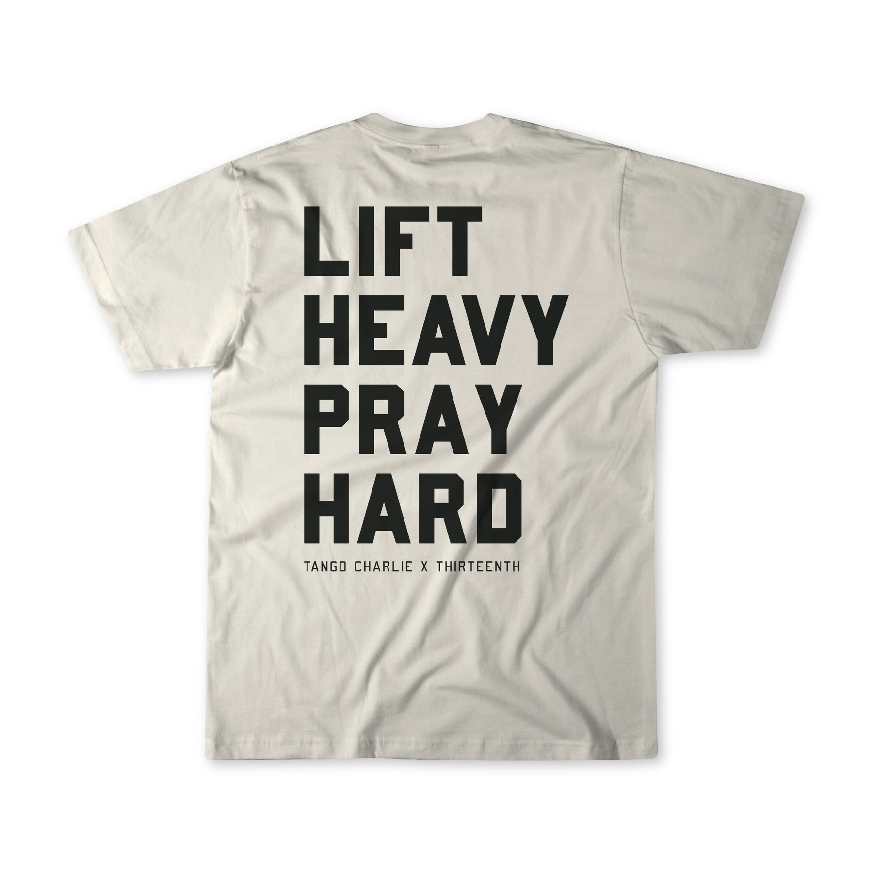 A light gray Lift Heavy. Pray Hard. - Tee from Tango Charlie Apparel, shown from the back with bold black text LIFT HEAVY PRAY HARD and smaller TANGO CHARLIE X THIRTEENTH below, reflecting spiritual resilience.