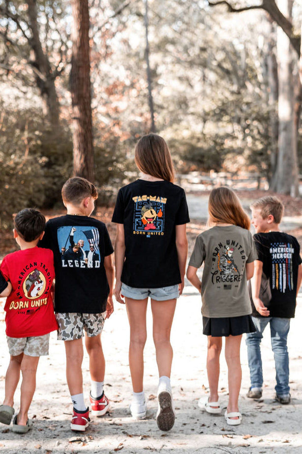 Five children stroll along a sandy forest path, wearing Youth Tac-Man graphic t-shirts from Born United Private Label. In shorts and tees available in youth sizes XS-XL, they enjoy a carefree day outdoors with trees as a lush backdrop.