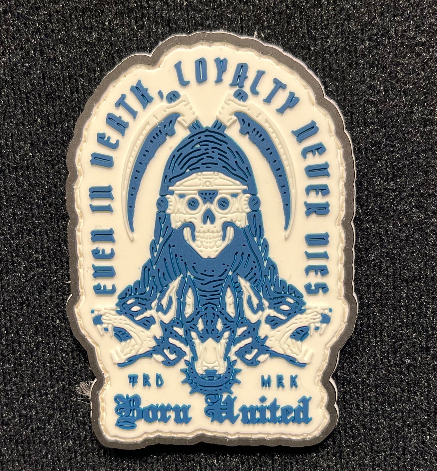The Loyalty PVC Patch by Born United Private Label features a skull-headed figure in a hood, encircled by animals on a blue and white background. The phrases Even in Death, Loyalty Never Dies and Born Limited adorn the patch.