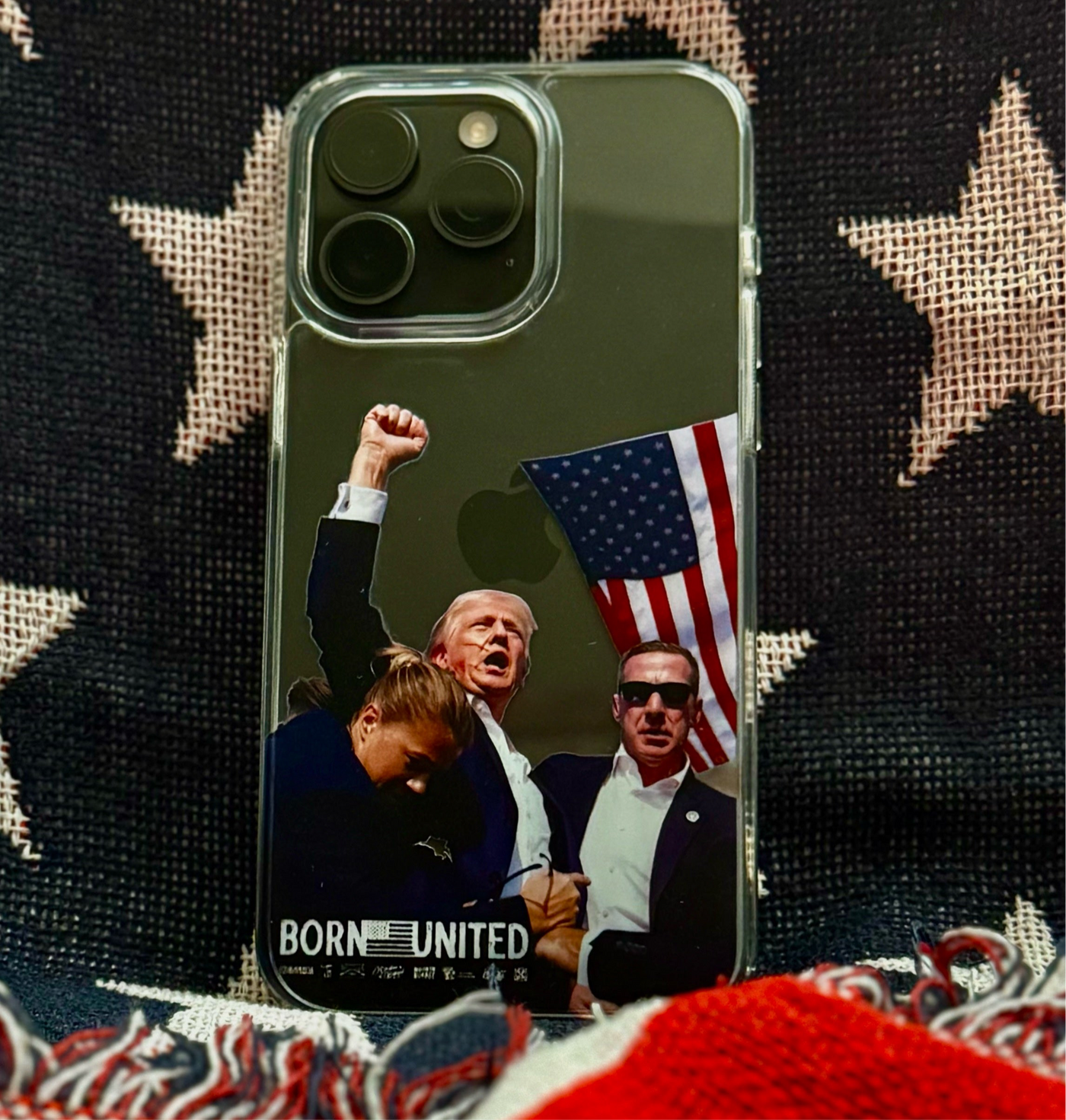 A Forever Legend iPhone Case by Born United Private Label sits on star-spangled fabric, featuring three people—one with a raised fist and U.S. flag—and the bold words BORN UNITED.