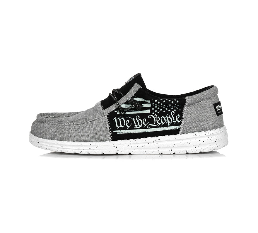 The Roam Split by Howitzer Clothing is a gray casual loafer with a white speckled sole and a side black patch featuring We the People in white text plus a partial U.S. flag design.