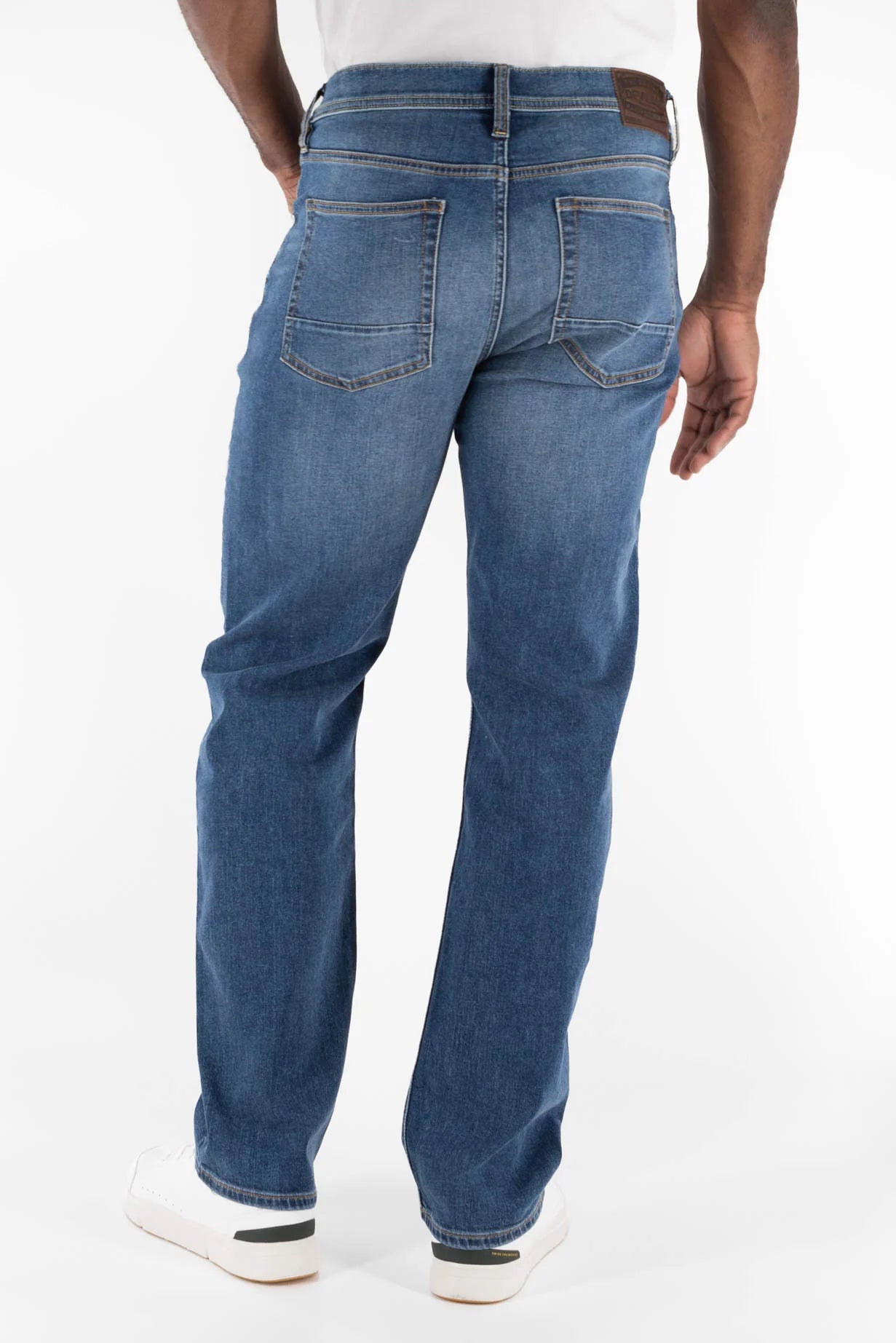 A person is shown from the back wearing Devil Dog Dungarees Relaxed Straight Jean - Bryson City with brown stitching and detailed back pockets, paired with white sneakers, against a plain white background.