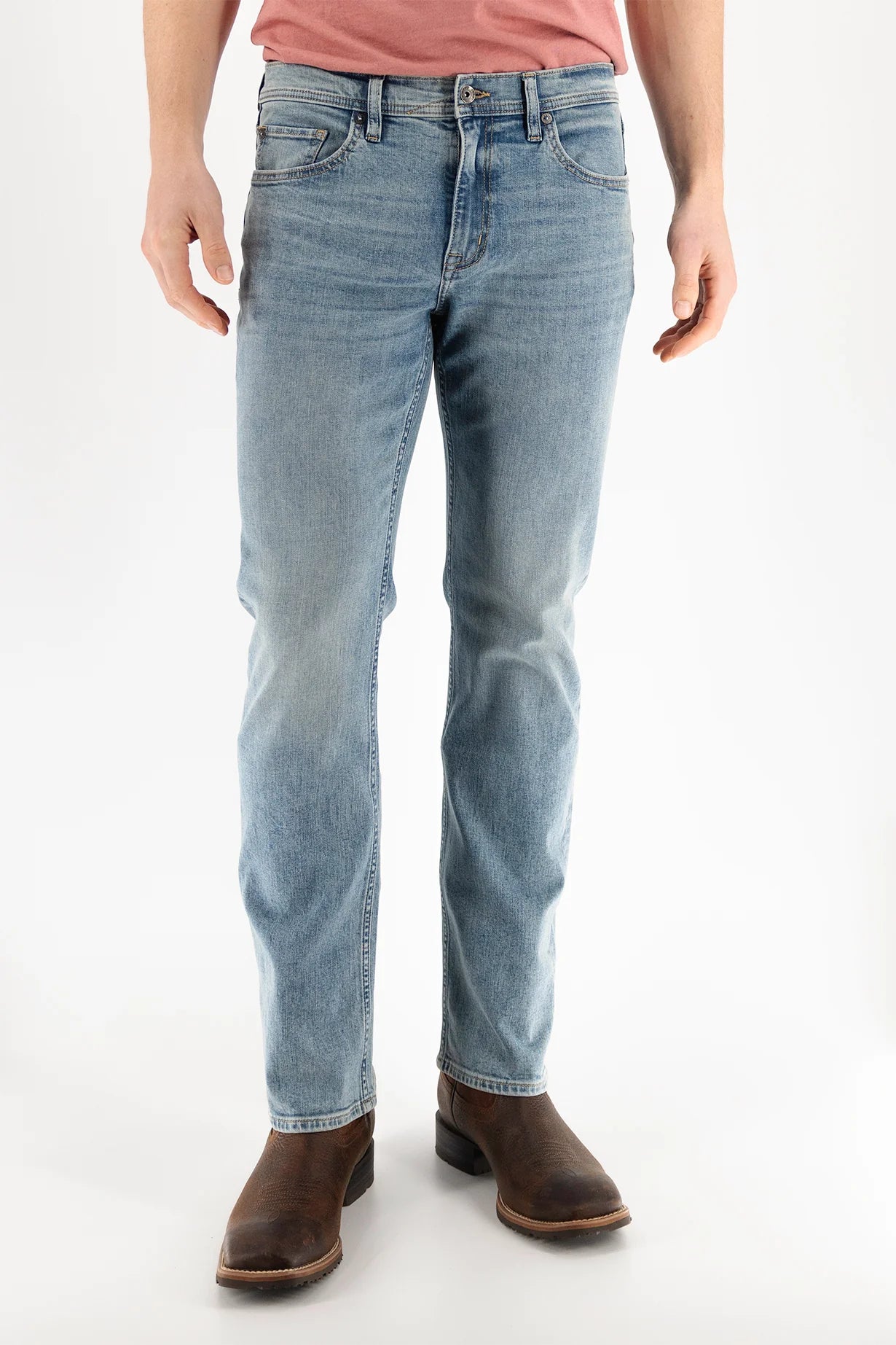 A person is wearing Devil Dog Dungarees Boot Cut Jean - Williamston in light blue, paired with a pink t-shirt and brown leather boots, standing against a plain white background. The photo is cropped from the shoulders down.