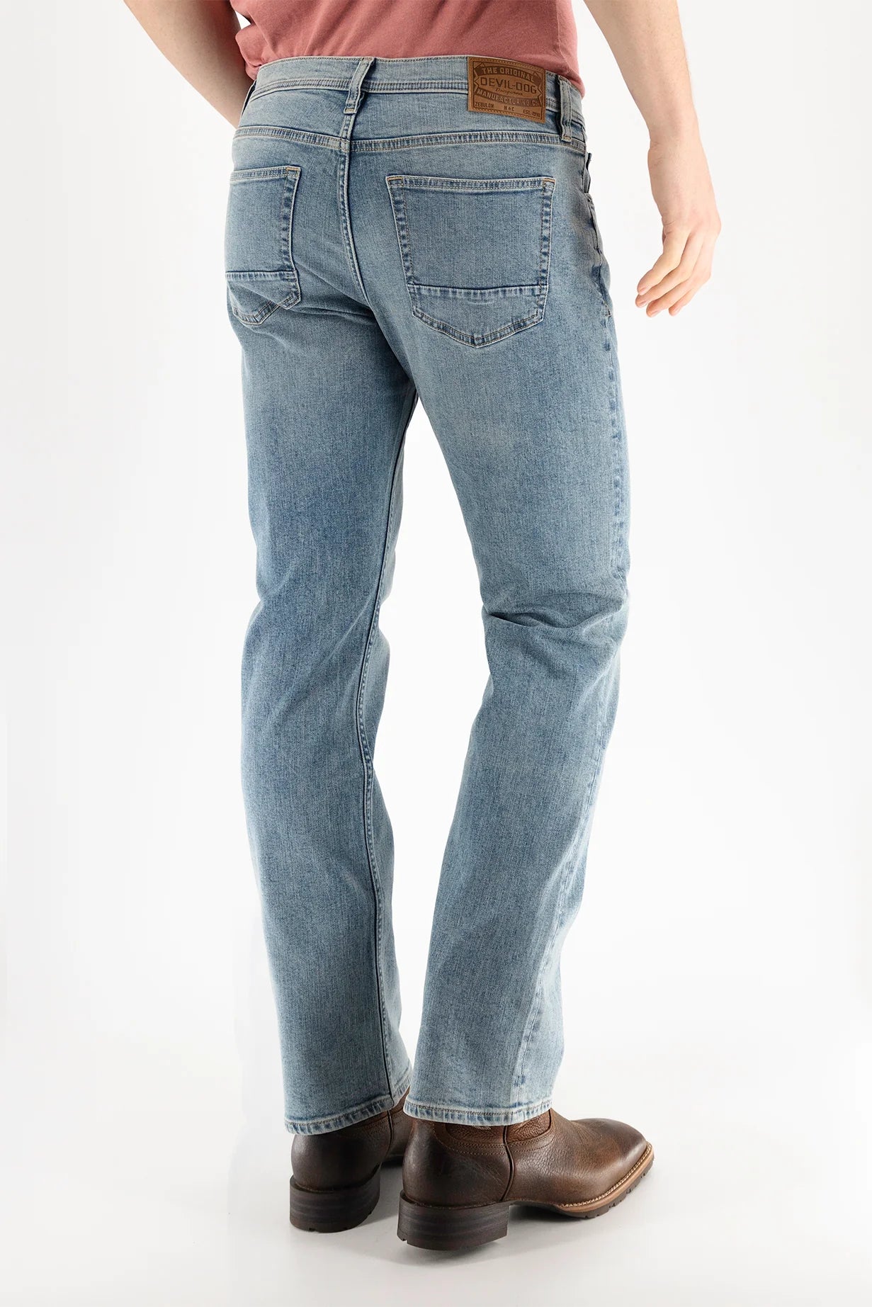 A person is seen from the back wearing Devil Dog Dungarees Boot Cut Jean - Williamston, styled with a pink shirt and brown boots, standing against a plain white background to highlight the jeans.