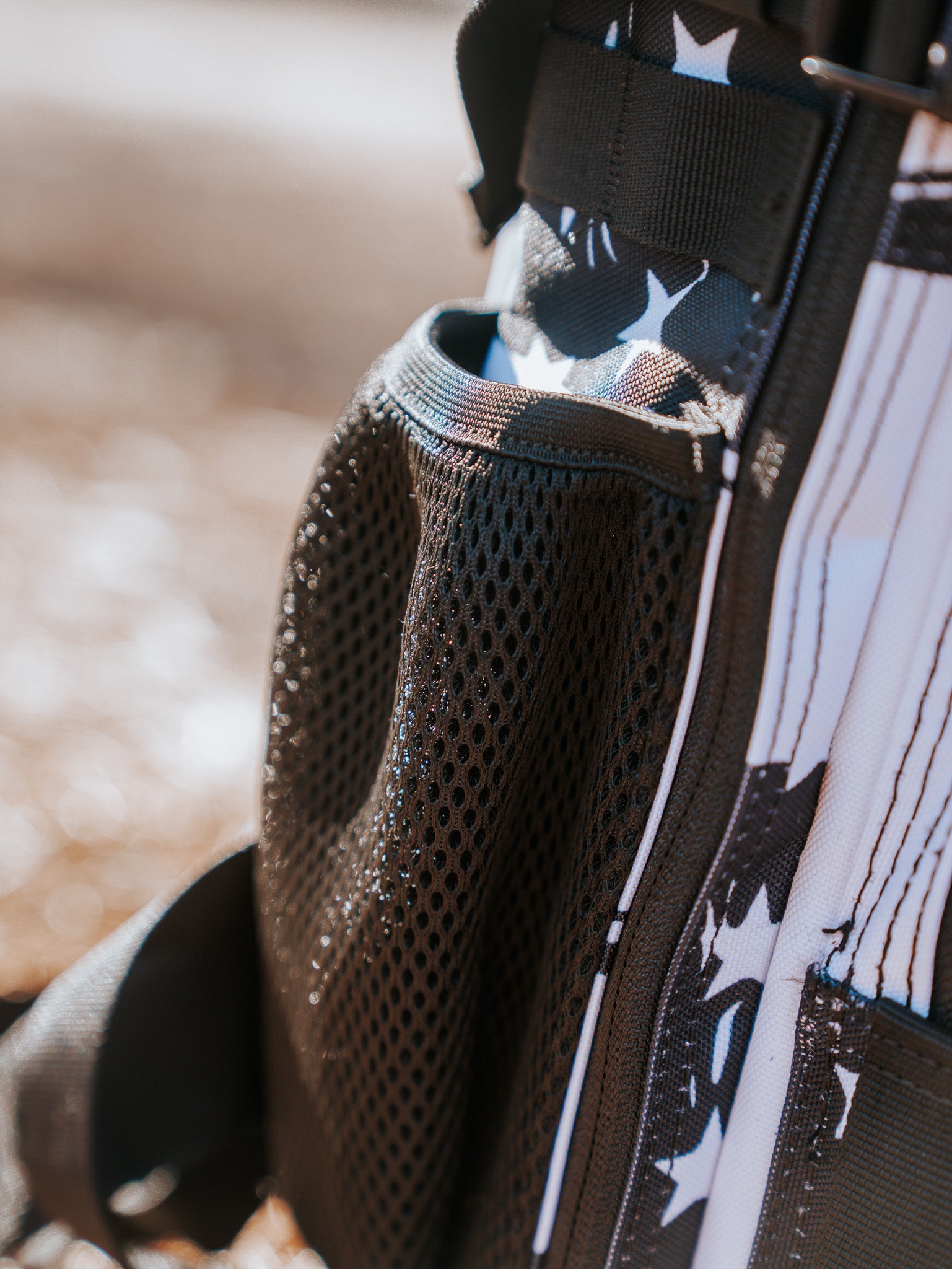 A close-up of the black mesh side pocket on the American Stealth Special Edition Tac-Pac - 25L by Born United Private Label emanates stealth vibes. Sunlight accentuates its texture, channeling the essence of stealth attire. The blurred background emphasizes this fashion-forward backpacks intricate details.