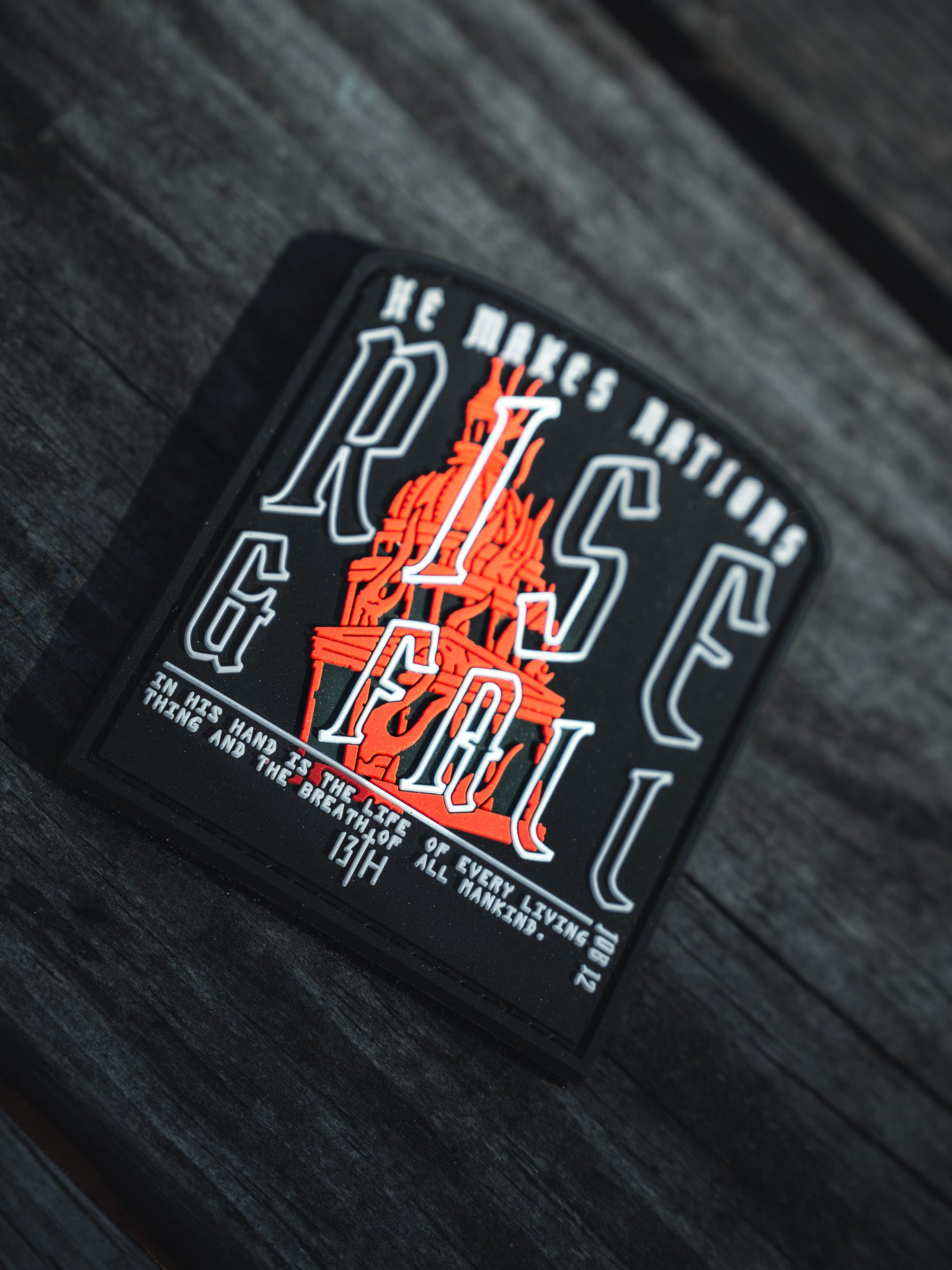 A black PVC patch from 13th, titled Rise And Fall, features an orange and black statue illustration with the phrase He makes nations rise and fall, alluding to thirteenth-century divine themes.