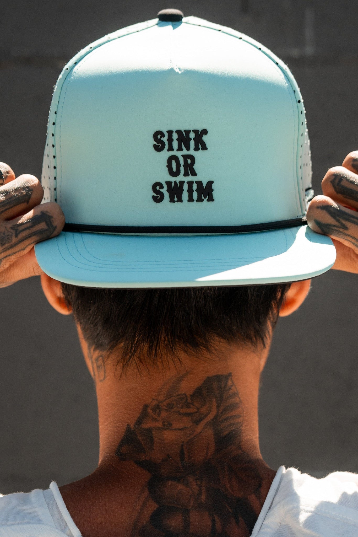 With their back to the camera, this person embodies the pirate life in a Relentless Betrayals Sink or Swim Seafoam PVC Snapback. Tattoos grace their neck and hands as they adjust the cap—a true testament to adventure and resilience.