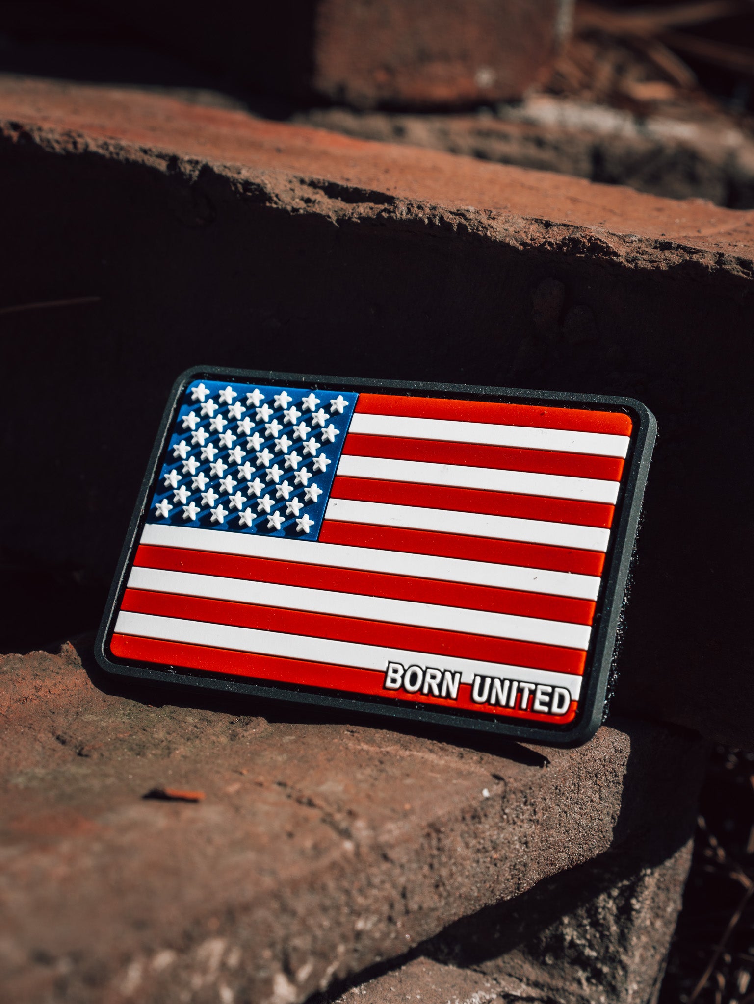 The American Flag PVC Patch from Born United Private Label, featuring a durable hook & loop design, proudly sits on rustic brick steps, showcasing its waterproof and washable features.