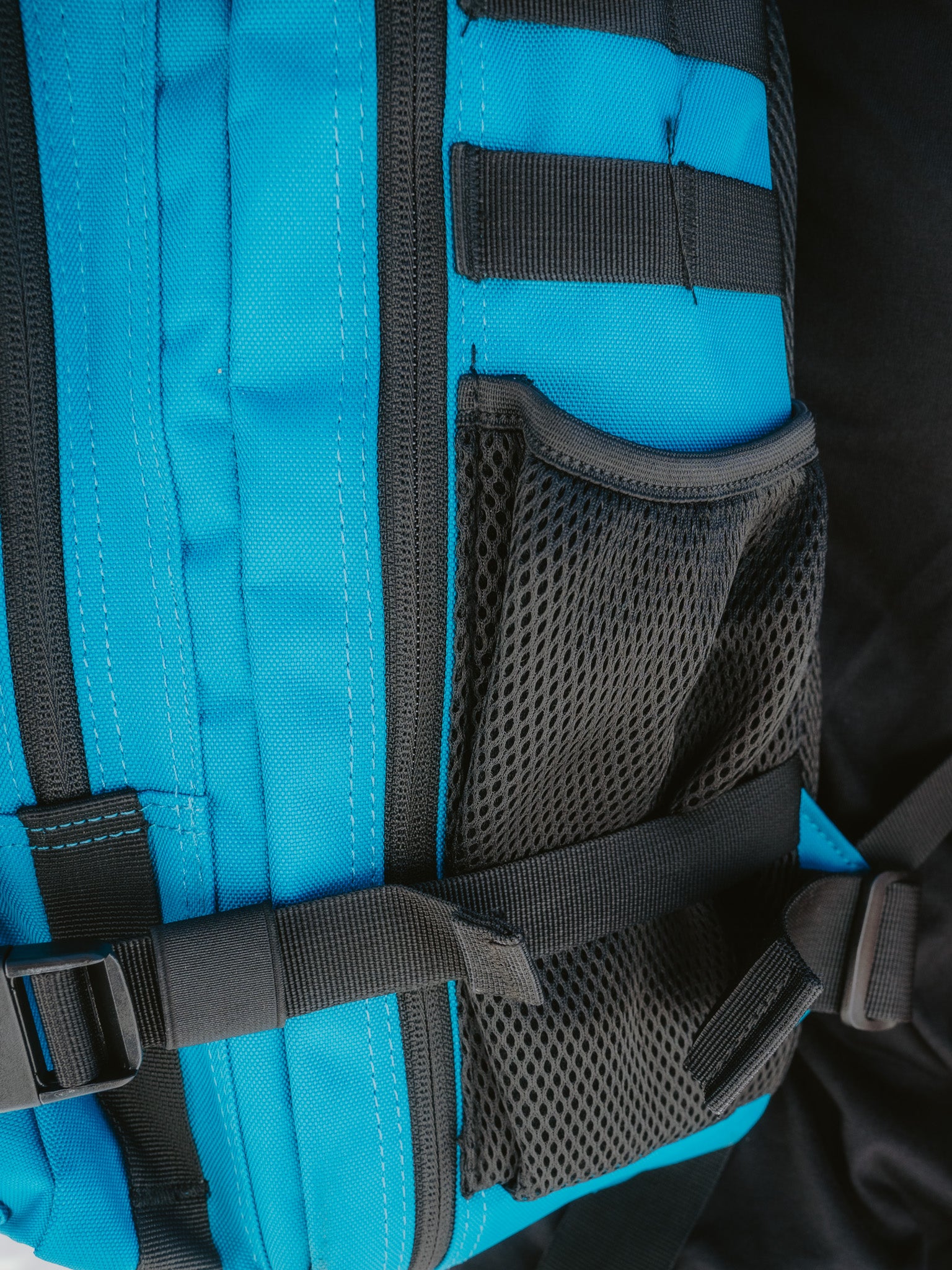 Close-up of the Electric Blue Premium Tac-Pac - 45L by Born United Private Label shows a durable electric blue and black backpack, featuring a mesh pocket, adjustable strap with buckle, and black stitching/details on vibrant blue sections.