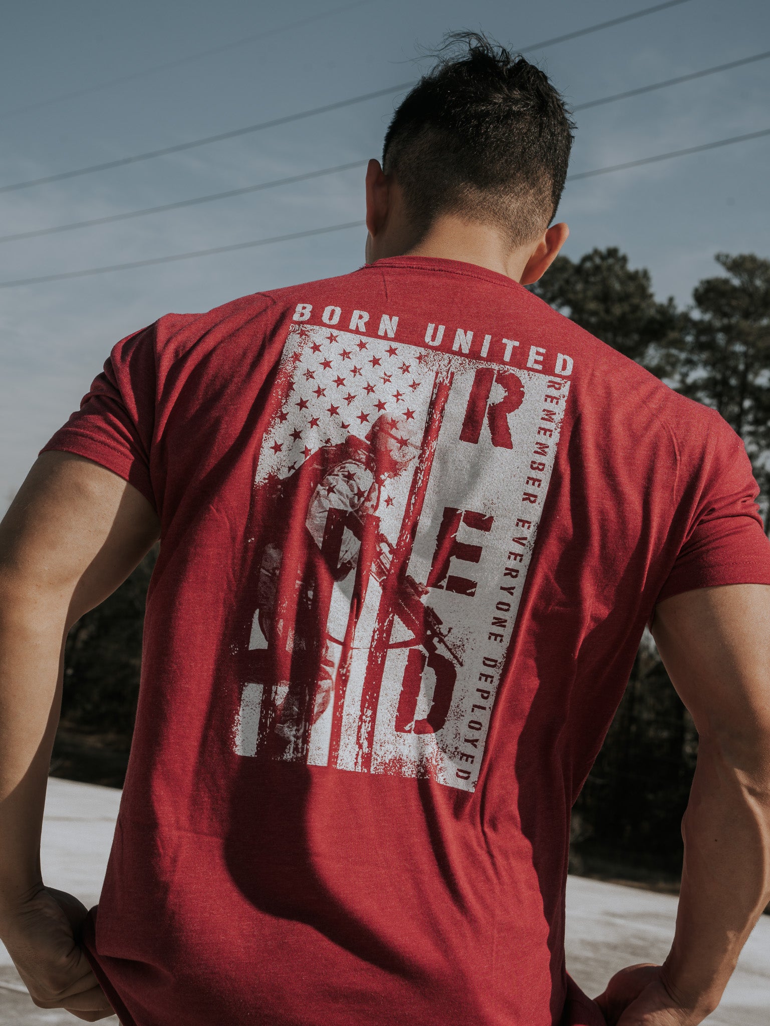 Someone outdoors wears a R.E.D. Friday shirt by Born United Private Label, featuring military-style graphics with BORN UNITED and R.E.D. Remember Everyone Deployed, honoring brave soldiers with a stylized flag and soldier image, celebrating the spirit of patriotism and freedom.