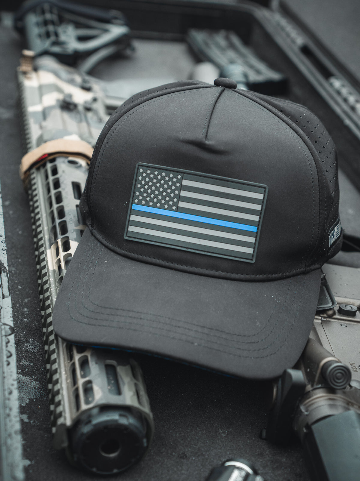 The Born United Premium Flag Snapback - TBL by Born United Private Label, featuring a black and white flag with a thin blue line, sits on a firearms case against a blurred background, symbolizing support for law enforcement.