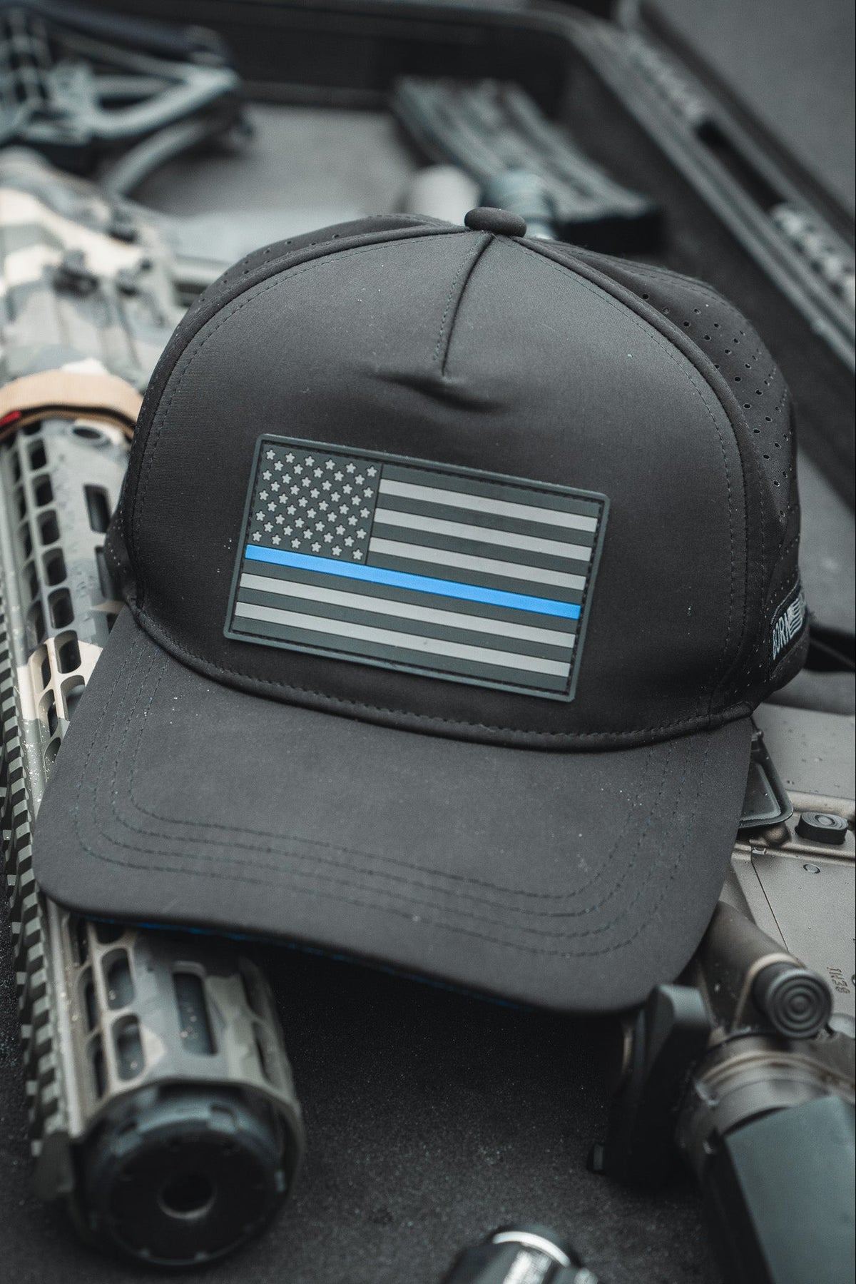 The Born United Premium Flag Snapback - TBL by Born United Private Label, featuring a black and white flag with a thin blue line, sits on a firearms case against a blurred background, symbolizing support for law enforcement.