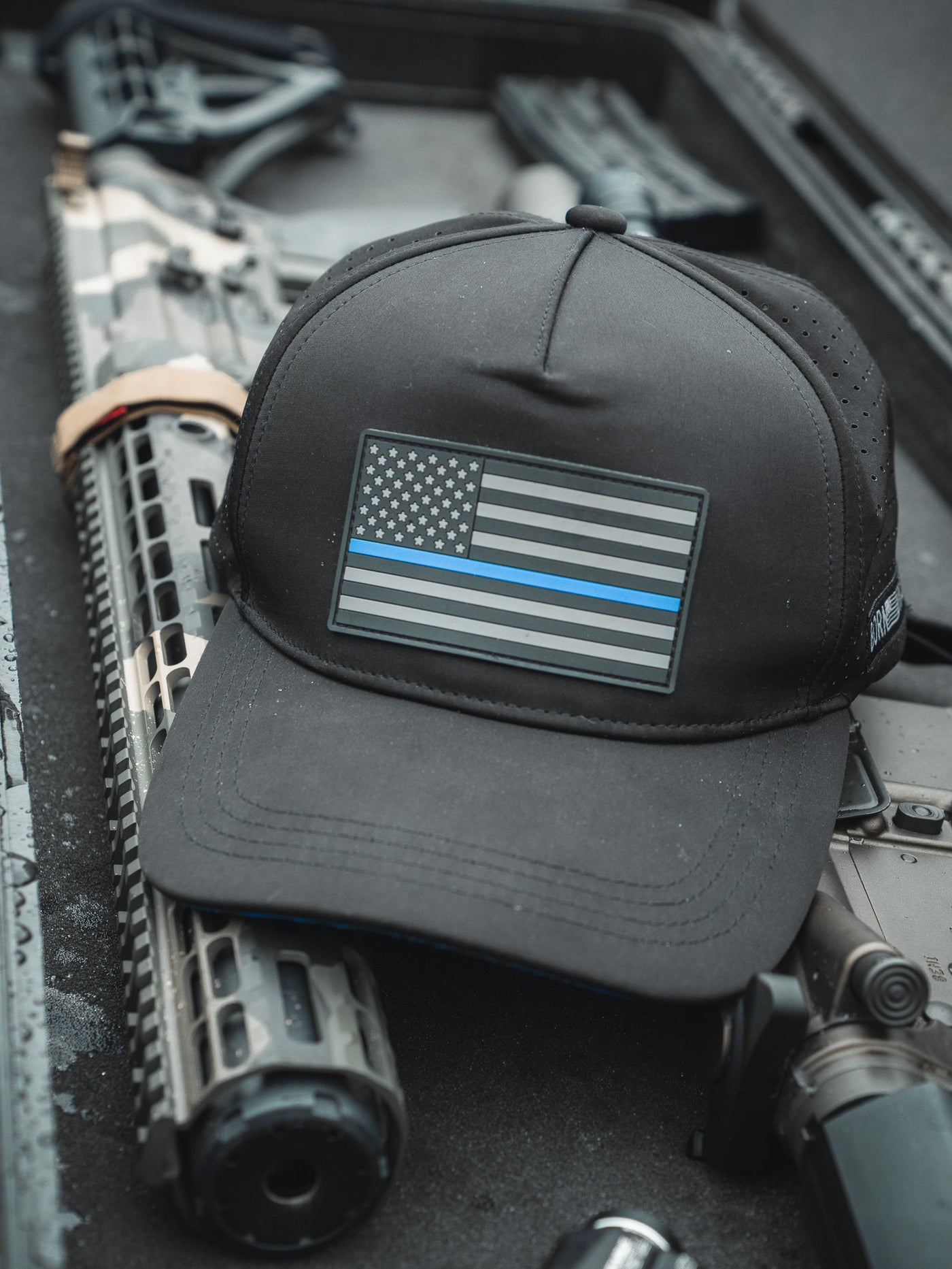 The Born United Premium Flag Snapback - TBL by Born United Private Label, featuring a black and white flag with a thin blue line, sits on a firearms case against a blurred background, symbolizing support for law enforcement.