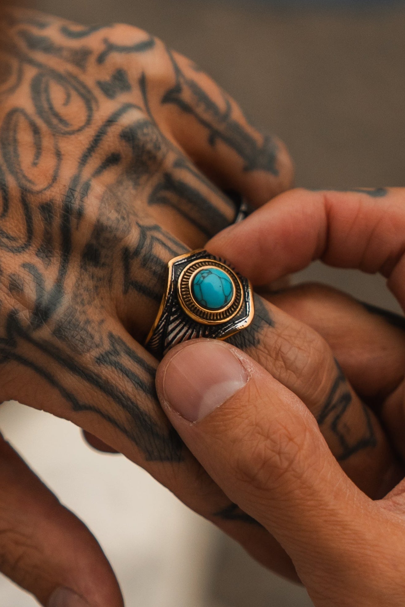 A close-up shows a tattooed hand slipping on Relentless Betrayals handcrafted Royal Crest Ring, featuring a decorative gold and black setting that beautifully showcases the vivid turquoise stone.