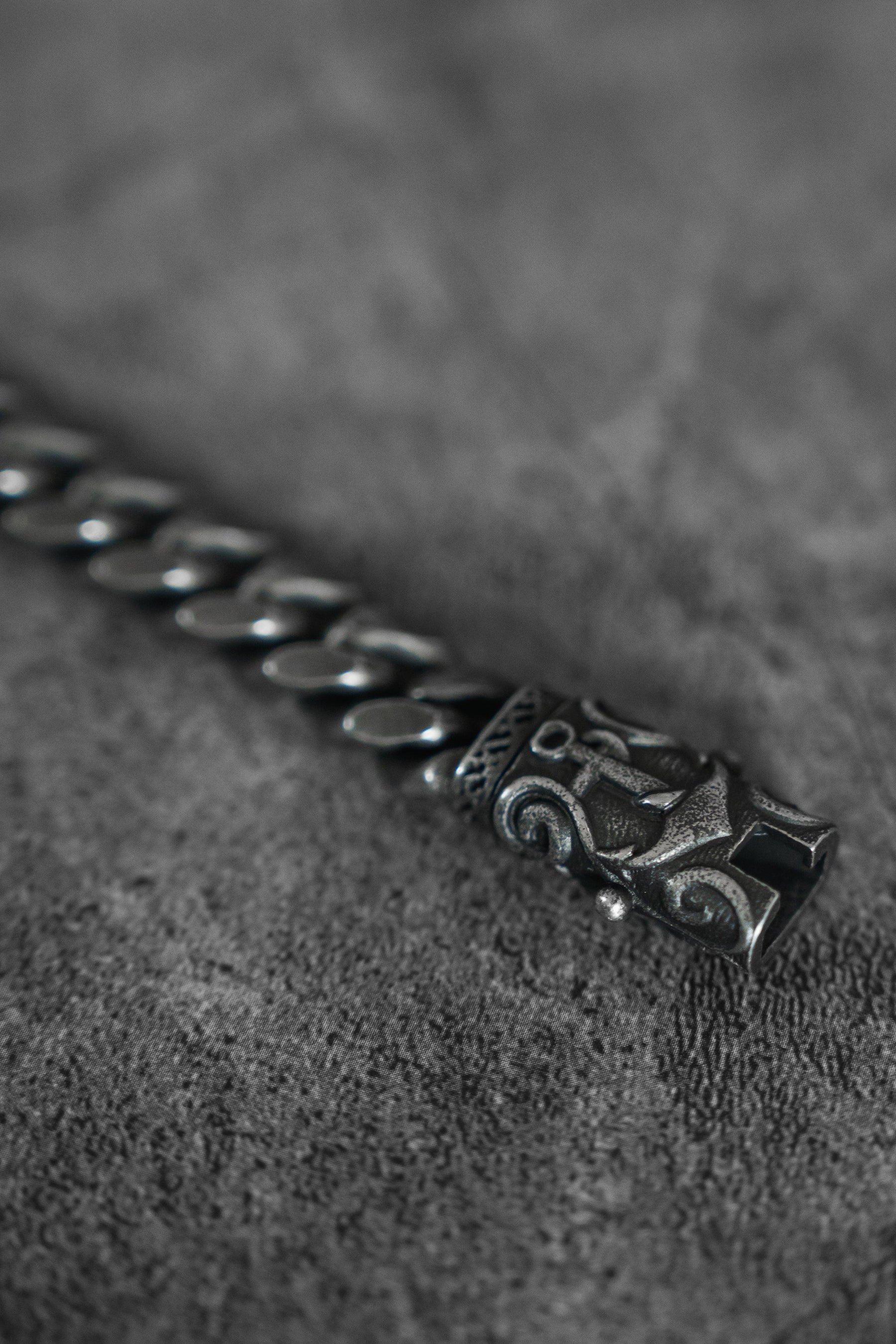 A close-up of the handcrafted Relentless Betrayals Voyager Bracelet, showcasing a textured metal design and decorative clasp on a gray surface. Its linked chain style and intricate engraving evoke maritime journeys and sea adventures.