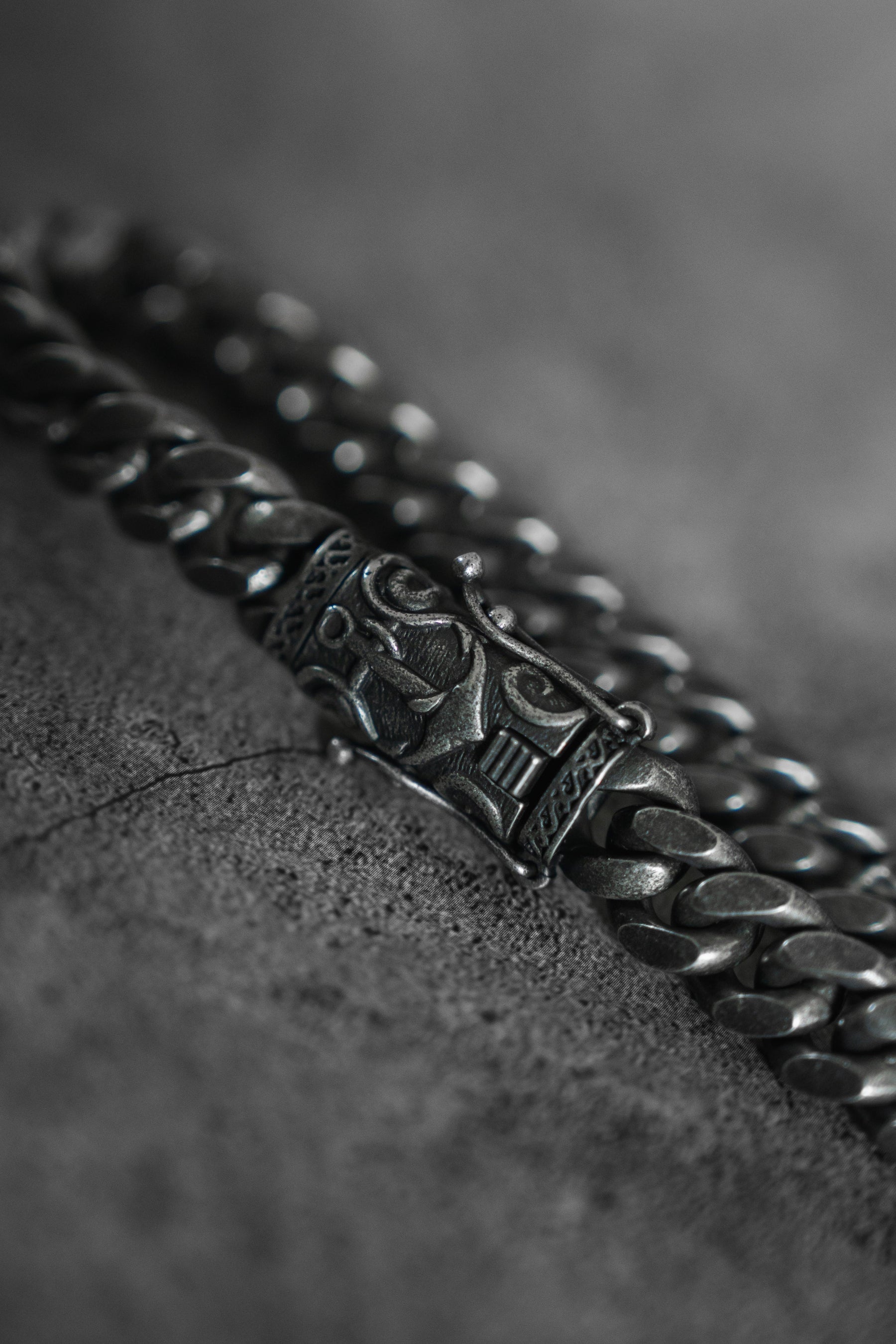 Close-up of the silver Voyager Bracelet by Relentless Betrayal, highlighting the intricate clasp details. The textured gray background, slightly blurred, enhances the metallic sheen and exquisite craftsmanship of this handcrafted jewelry piece.