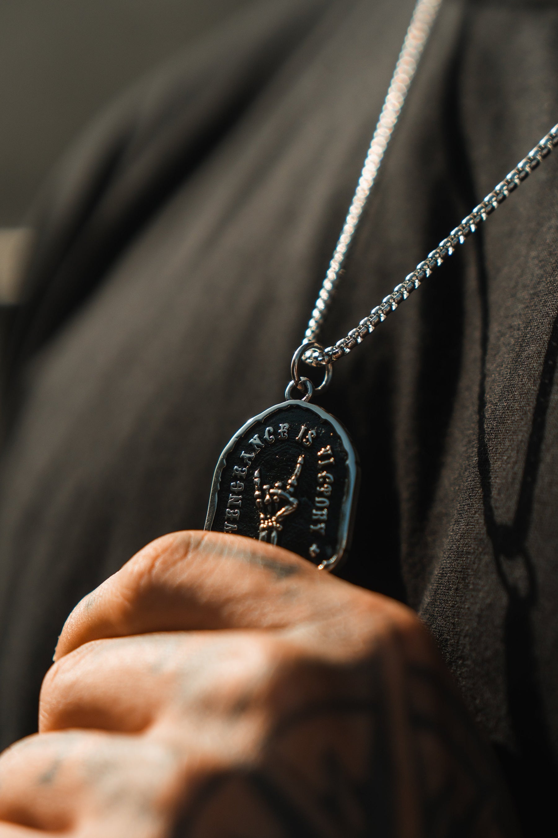 A person proudly wears the Vengeance Necklace by Relentless Betrayal, featuring a raised fist symbol and the words Rock and Roll. With a black shirt and tattoos on display, they embody resilience and empowerment.