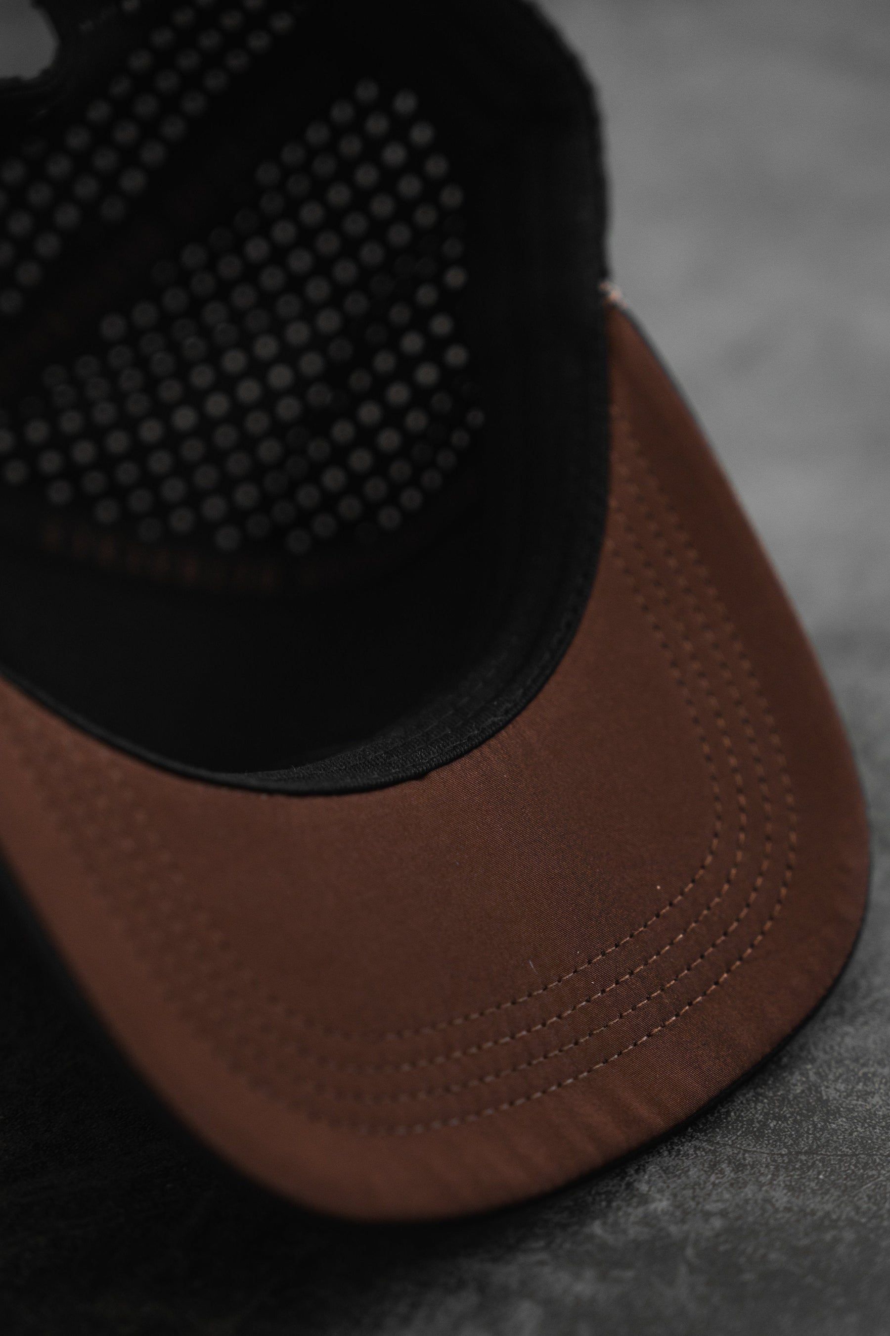 The Vengeance Snapback by Relentless Betrayal, featuring a sturdy brown exterior and black mesh interior, sits on a dark surface. Its forward-facing peak highlights the empowering stitching details along the brim.