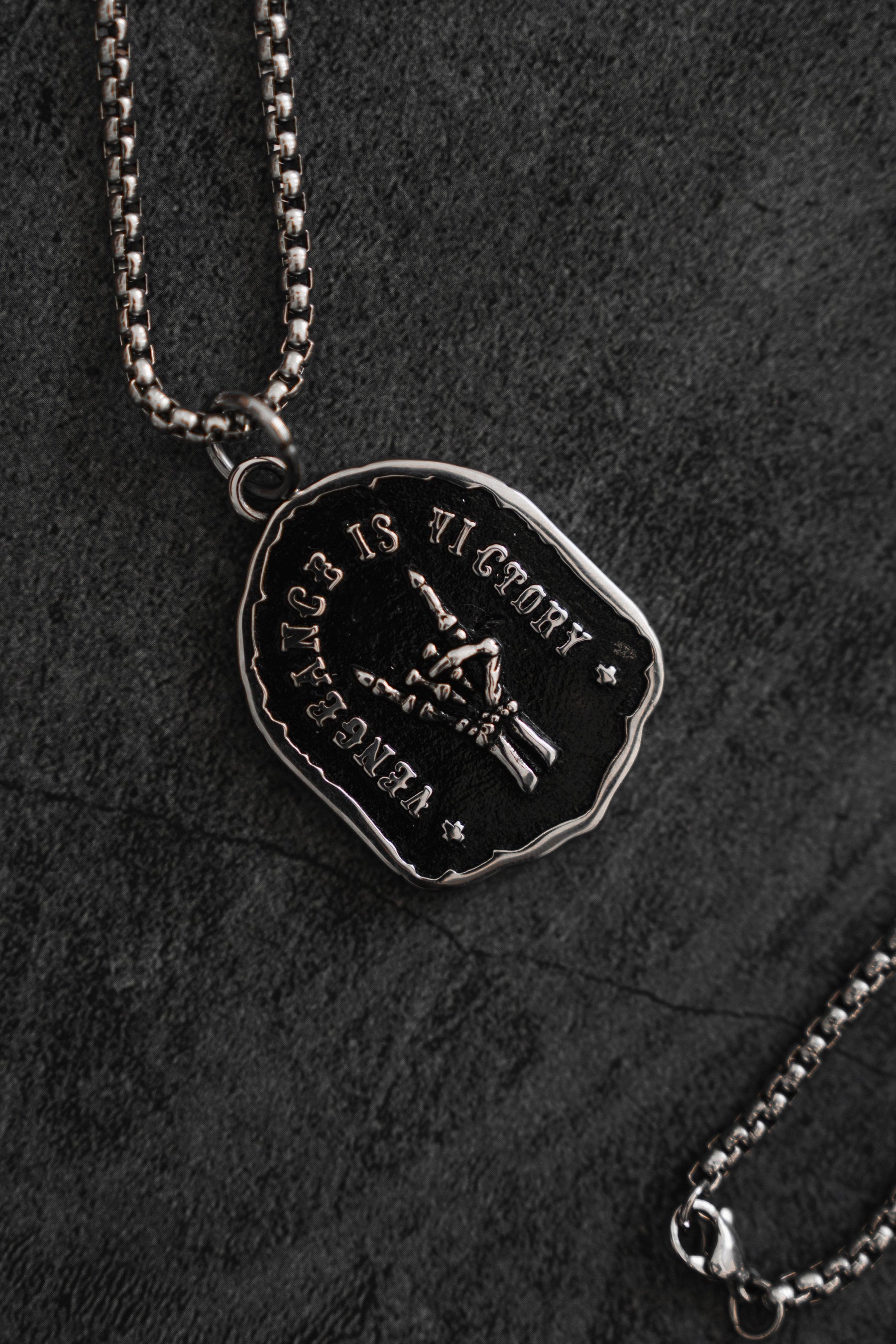 The Vengeance Necklace by Relentless Betrayal features a silver pendant with an eagle clutching arrows, surrounded by the powerful words Vengeance is Victory and Tyrants, all set on a dark, textured background to symbolize resilience and strength.