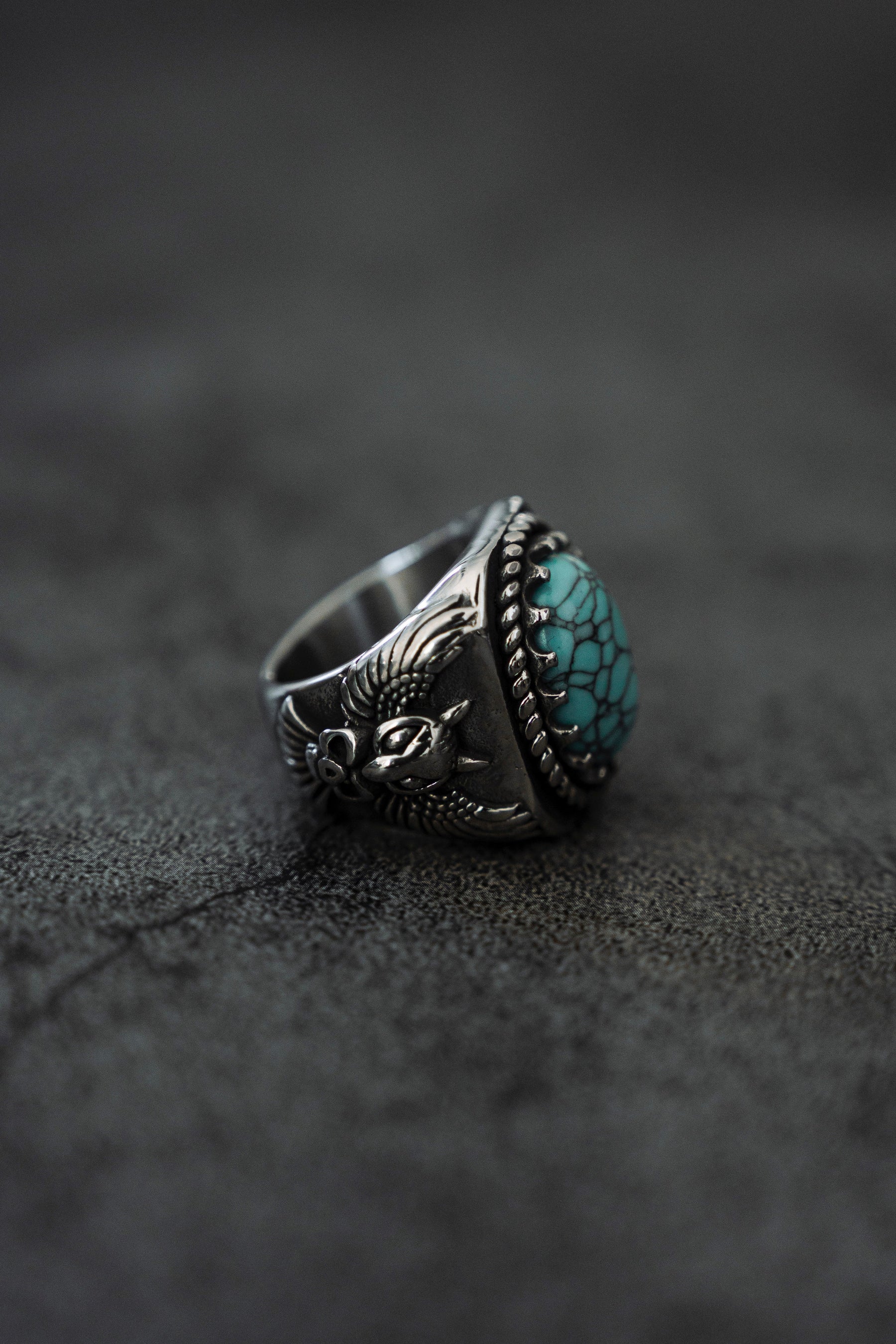 The Royal Guardian Ring by Relentless Betrayal is a handcrafted stainless-steel piece with a silver finish, featuring an intricate eagle design around a turquoise stone, evoking the elegance of an antique heirloom.