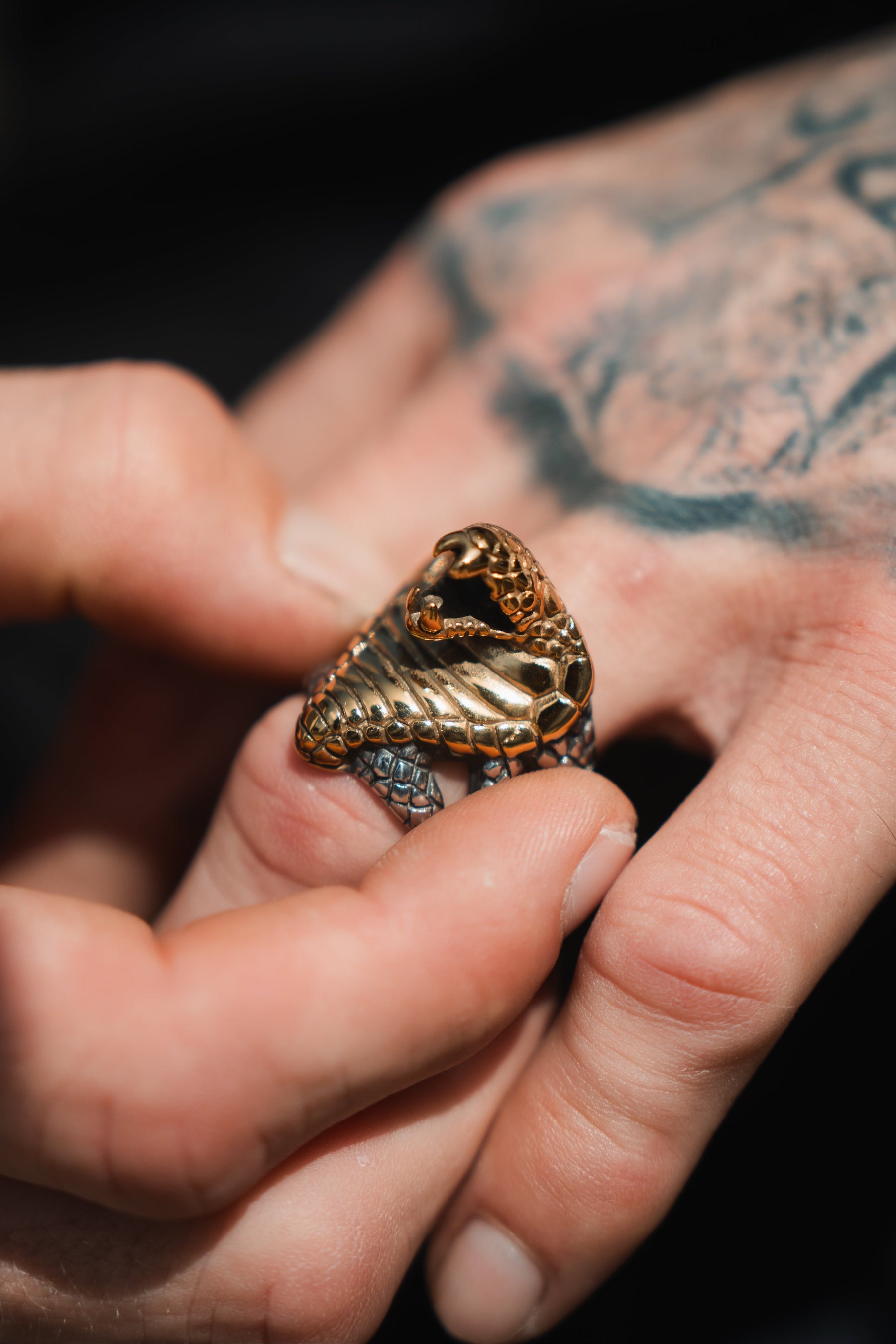 A tattooed hand adorns a handcrafted Cobra King Ring by Relentless Betrayal, intricately designed in stainless steel with a coiled snake motif.