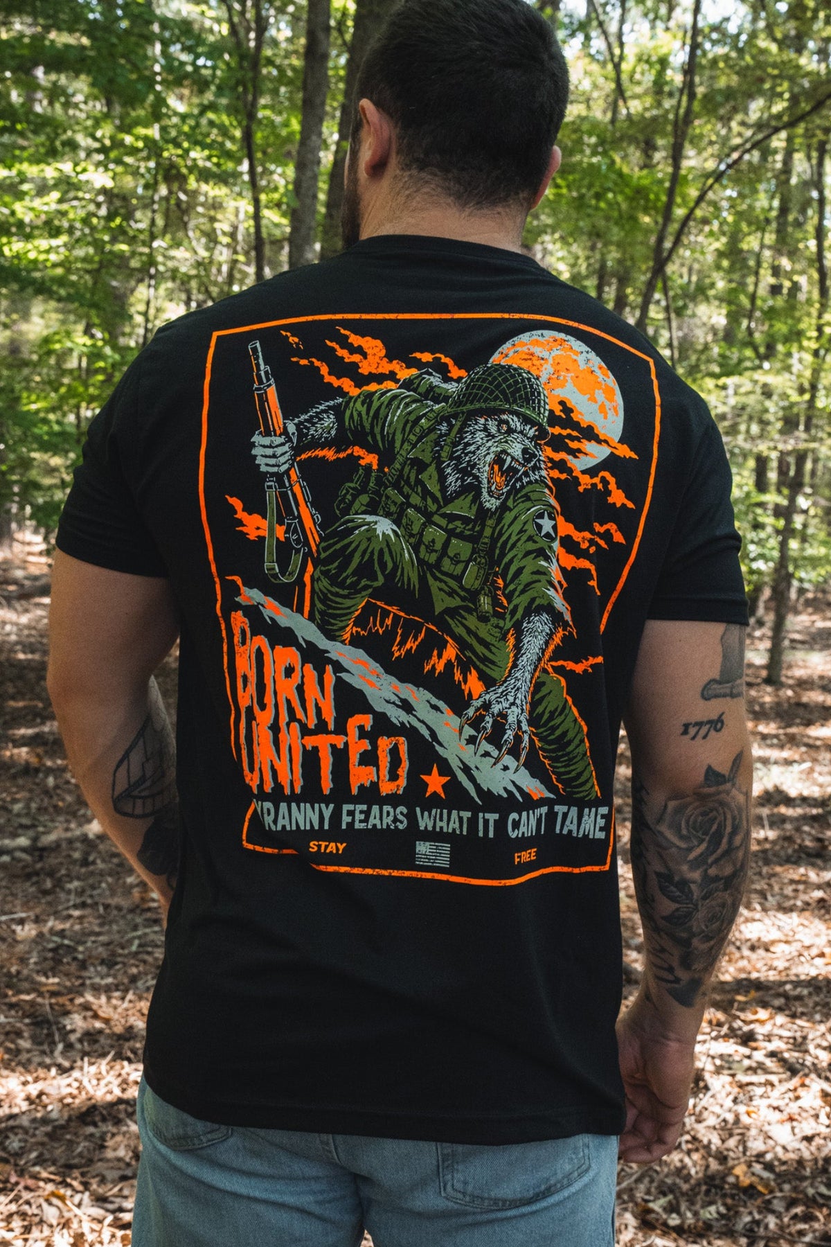 Back view of a person wearing a black Full Moon Tee, featuring a graphic of an armed werewolf in military gear, an orange full moon, and the text: Born United: Tyranny fears what it cant tame.