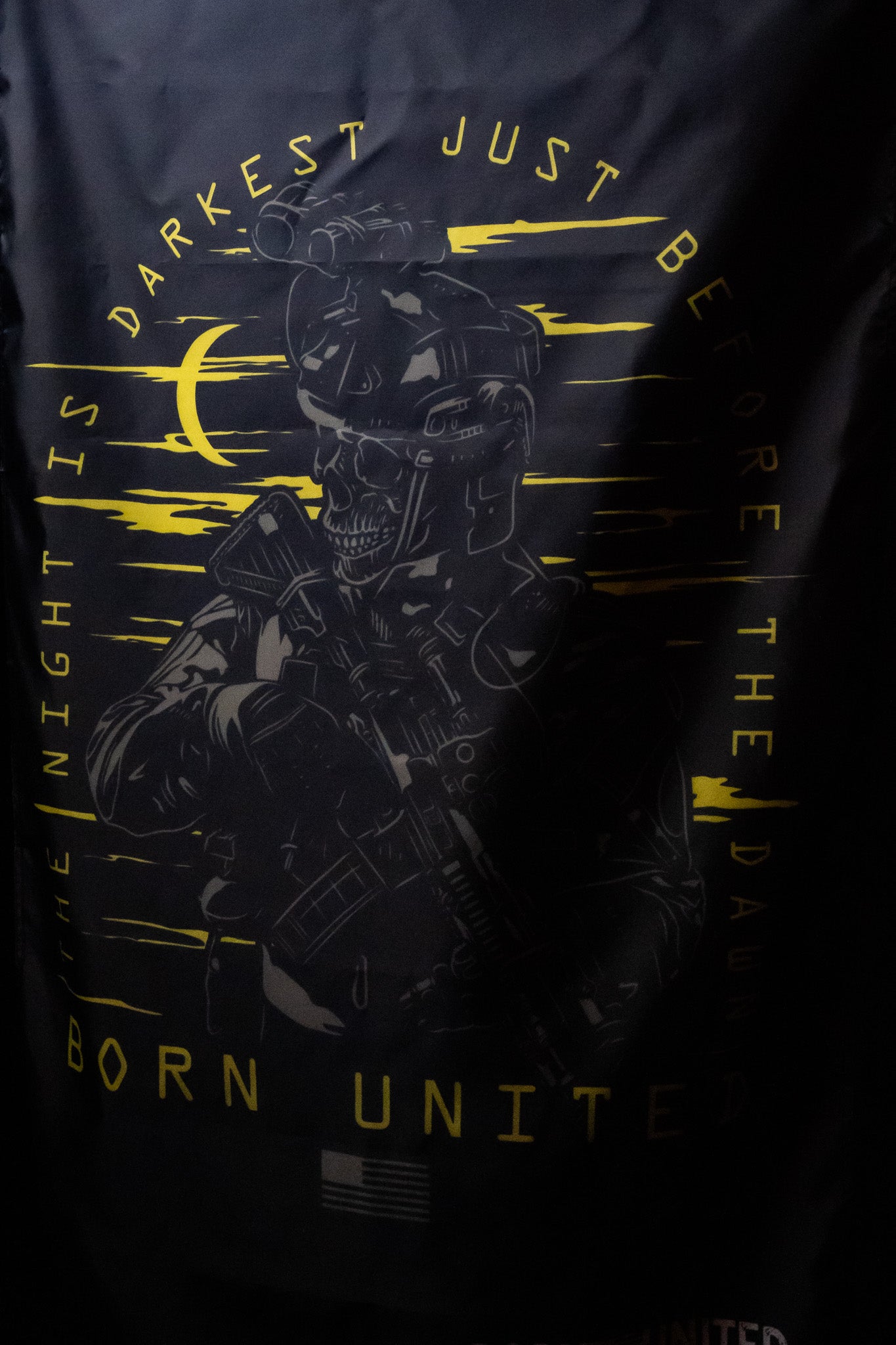 A skeleton in tactical gear with metal-grommeted polyester straps holds a rifle against a dark background on the Before Dawn Flag (Warehouse) by Born United Private Label. Text reads Born United. Night is Darkest. Neon yellow moon and sky elements illuminate the scene.