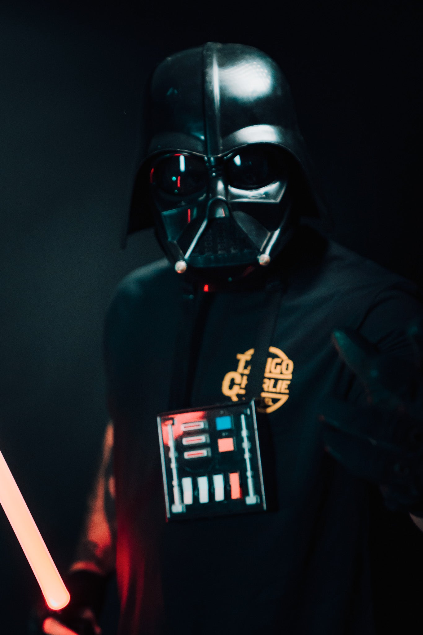 In a dimly lit setting, someone in a Lift Vader T-shirt by Tango Charlie Apparel wields a glowing red lightsaber. This limited edition piece is perfect for any science fiction enthusiast.