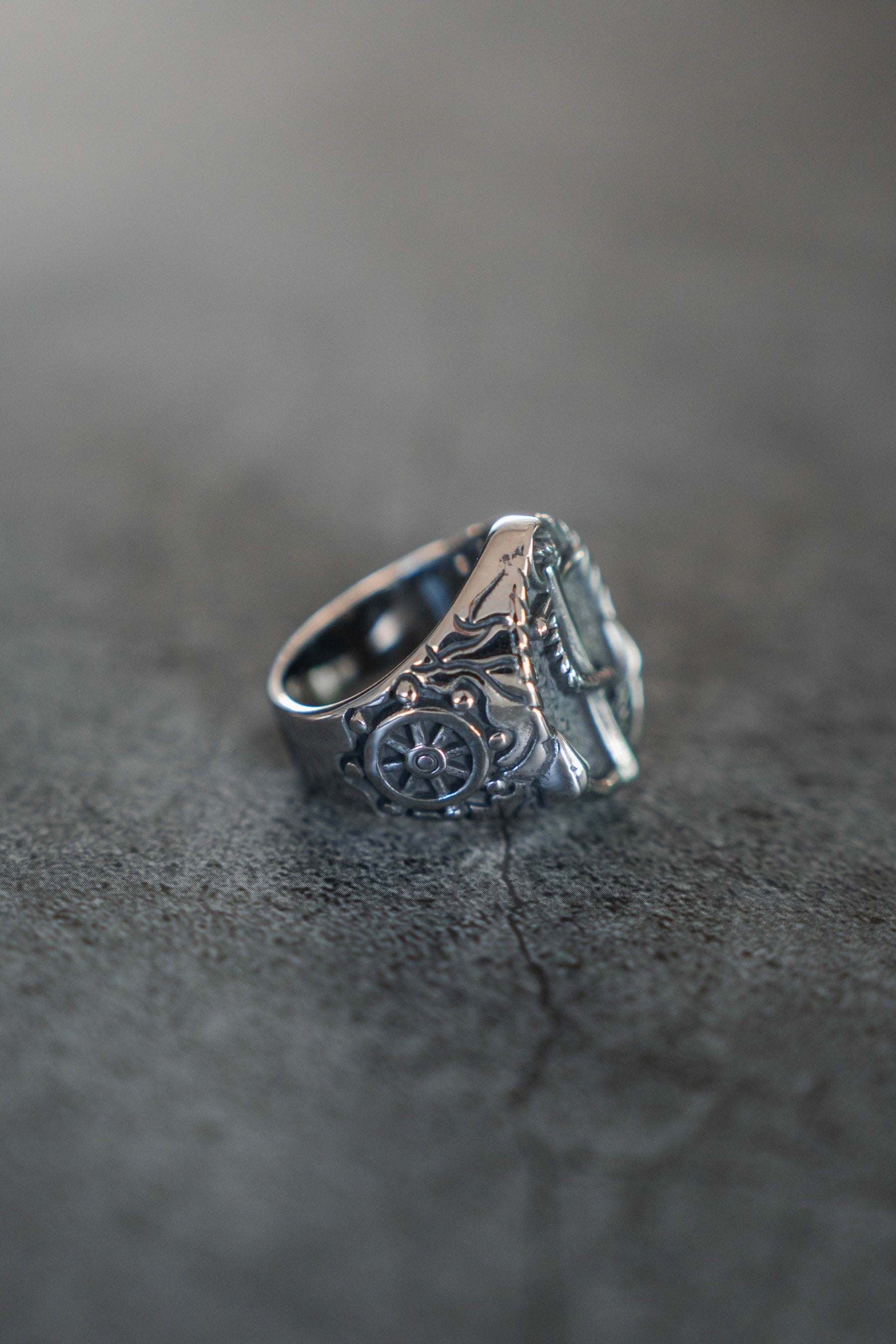 The Relentless Betrayal Voyager Ring, crafted from stainless steel with a compass design, showcases intricate craftsmanship against a textured dark gray surface, evoking adventure and exploration.