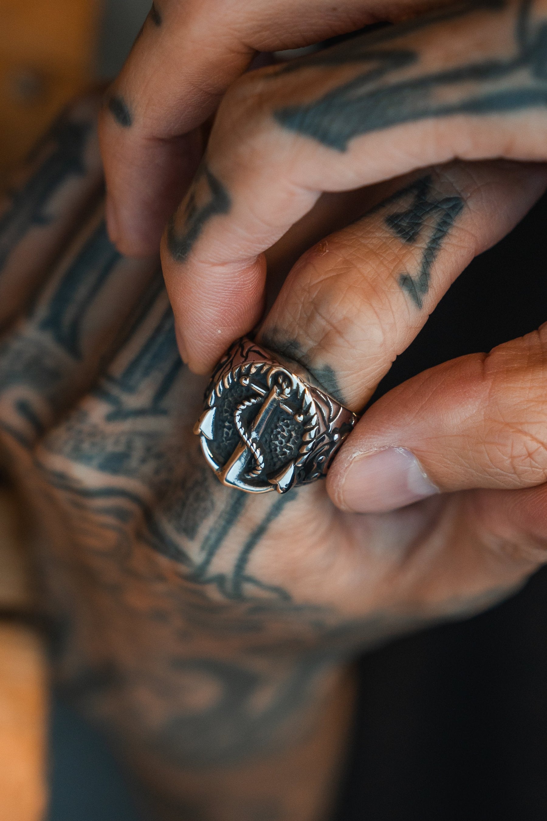 A tattooed hand grips the Relentless Betrayals Voyager Ring, a striking stainless steel piece with an anchor and rope design, ideal for adventure lovers. The intricate tattoos add unique flair to this captivating scene.