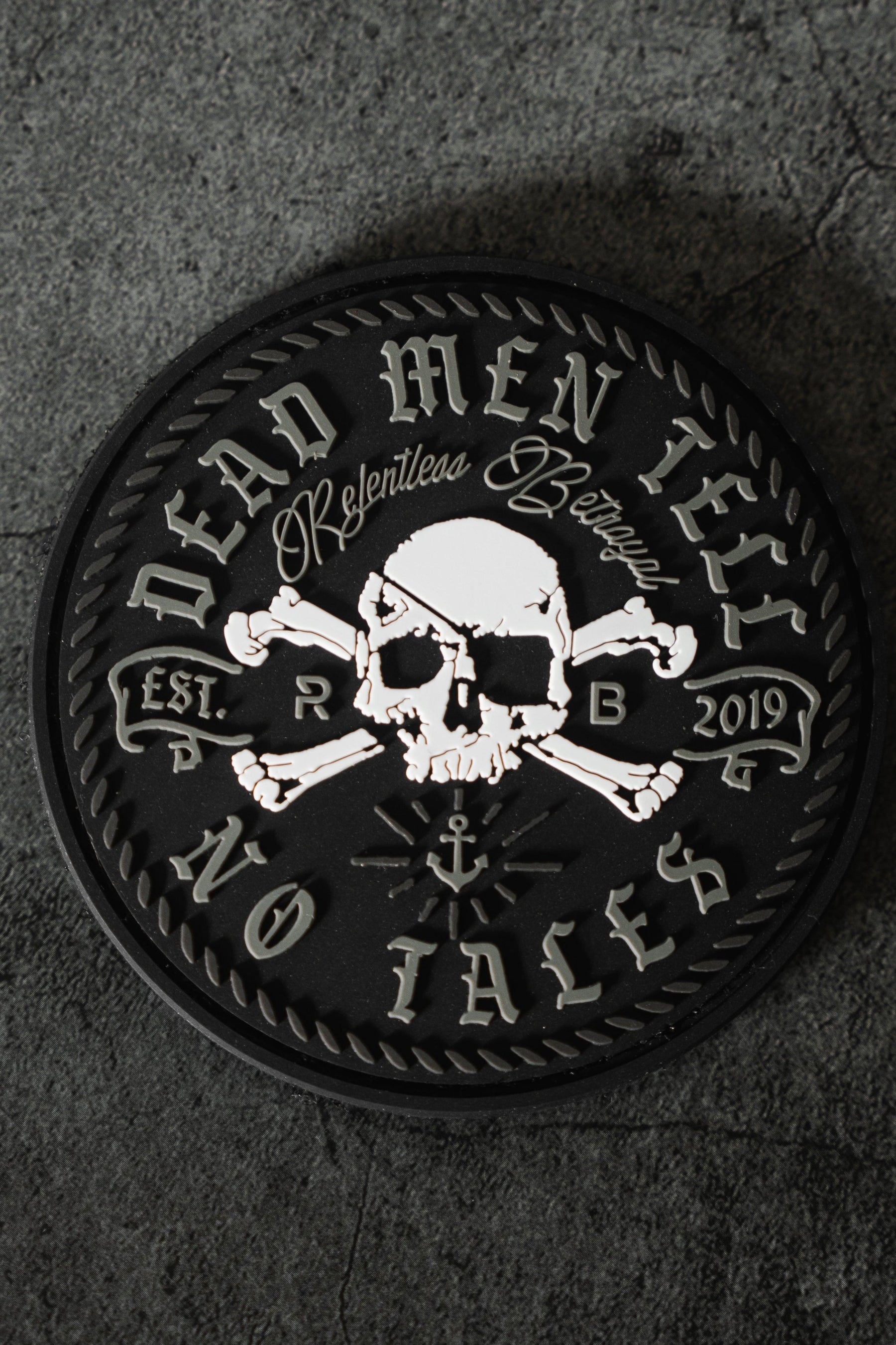The Tell No Tales Patch by Relentless Betrayal is a round black 3D PVC design featuring a skull and crossbones, Dead Men Tell No Tales, Relentless Betrayal, and Est. 2019 around the edge, initials R and B flanking the skull, with an anchor beneath—a perfect addition to any premium t-shirt.