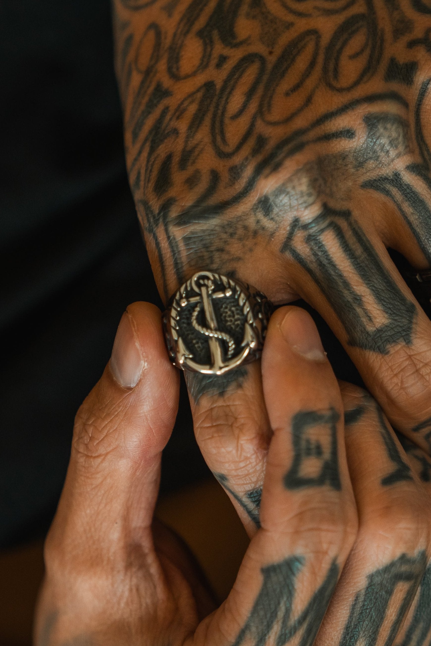 A close-up of tattooed hands showcases a Relentless Betrayal Voyager Ring. The stainless steel jewelry enhances intricate finger and hand tattoos featuring geometric shapes and bold lines.