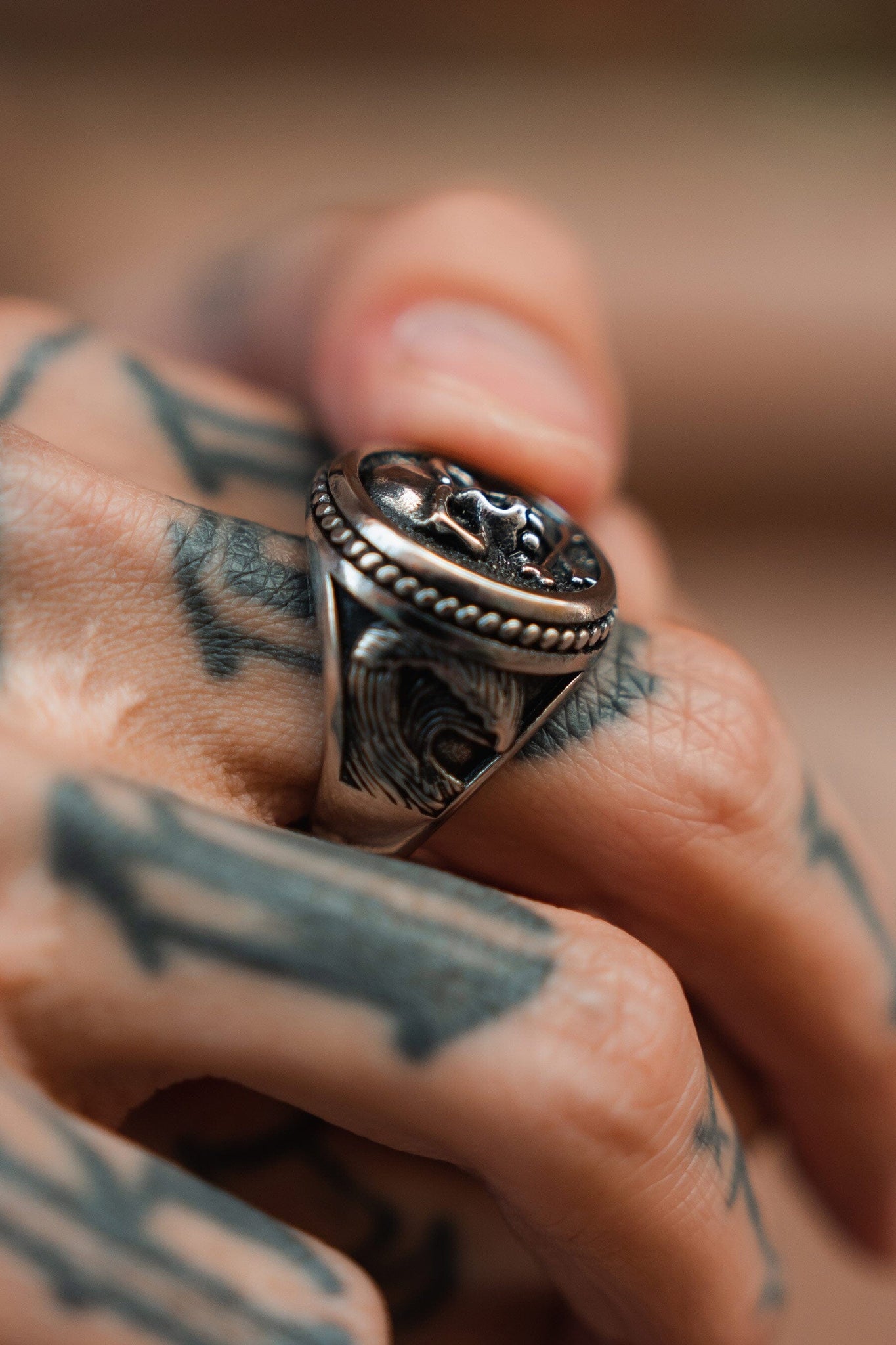 A close-up of a tattooed hand wearing the Relentless Betrayals Pirates Life Stainless Steel Ring, featuring a skull design that echoes the pirate lifestyle. The bold tattoos highlight the rings craftsmanship as the fingers curl slightly around this treasure.