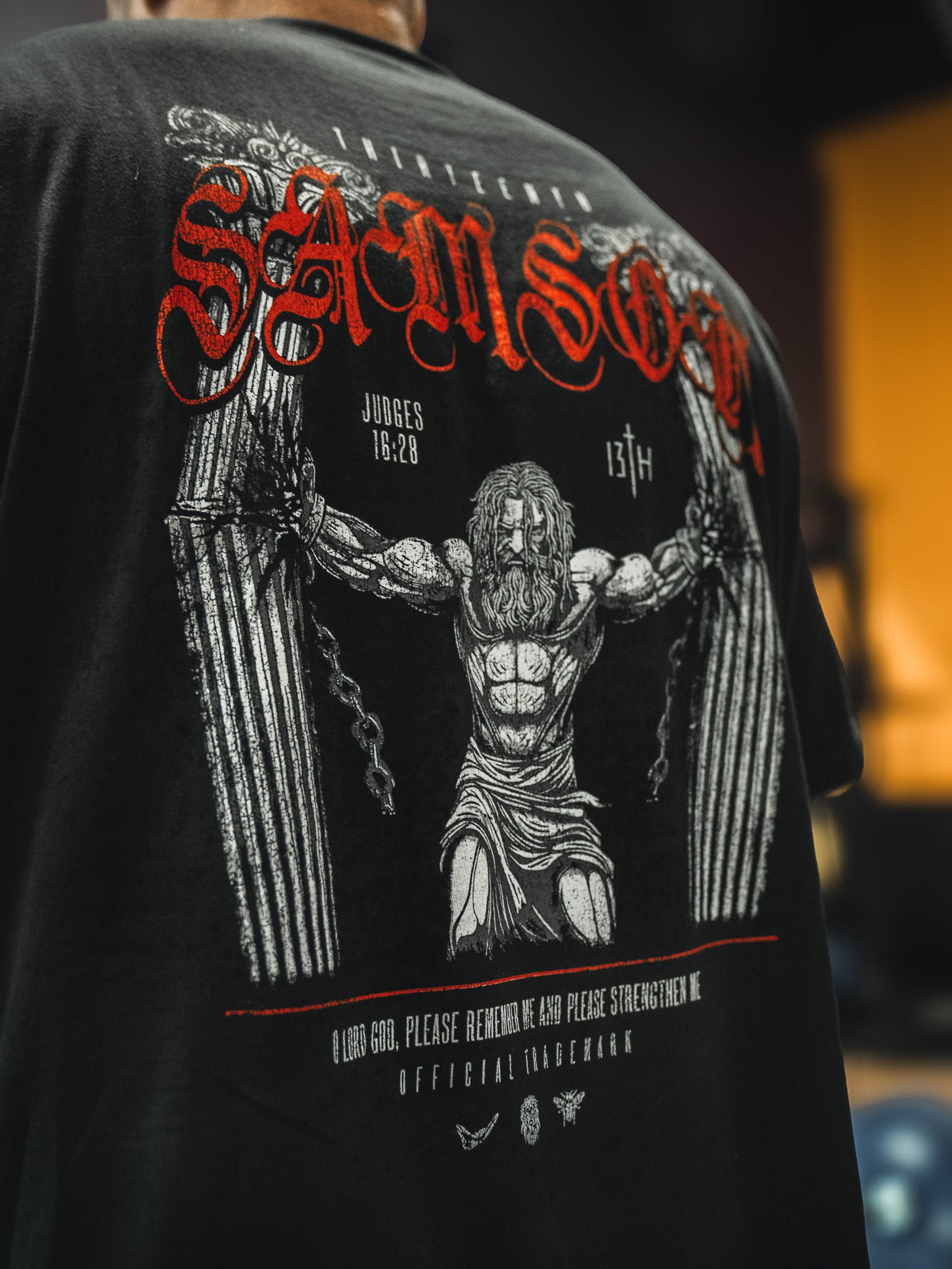 The 13th Samson Premium Tee is a bold, faith-inspired shirt showing muscular Samson breaking pillars, “SAMSON” in red above, and Judges 16:28 below—crafted with premium quality and detailed text and graphics.