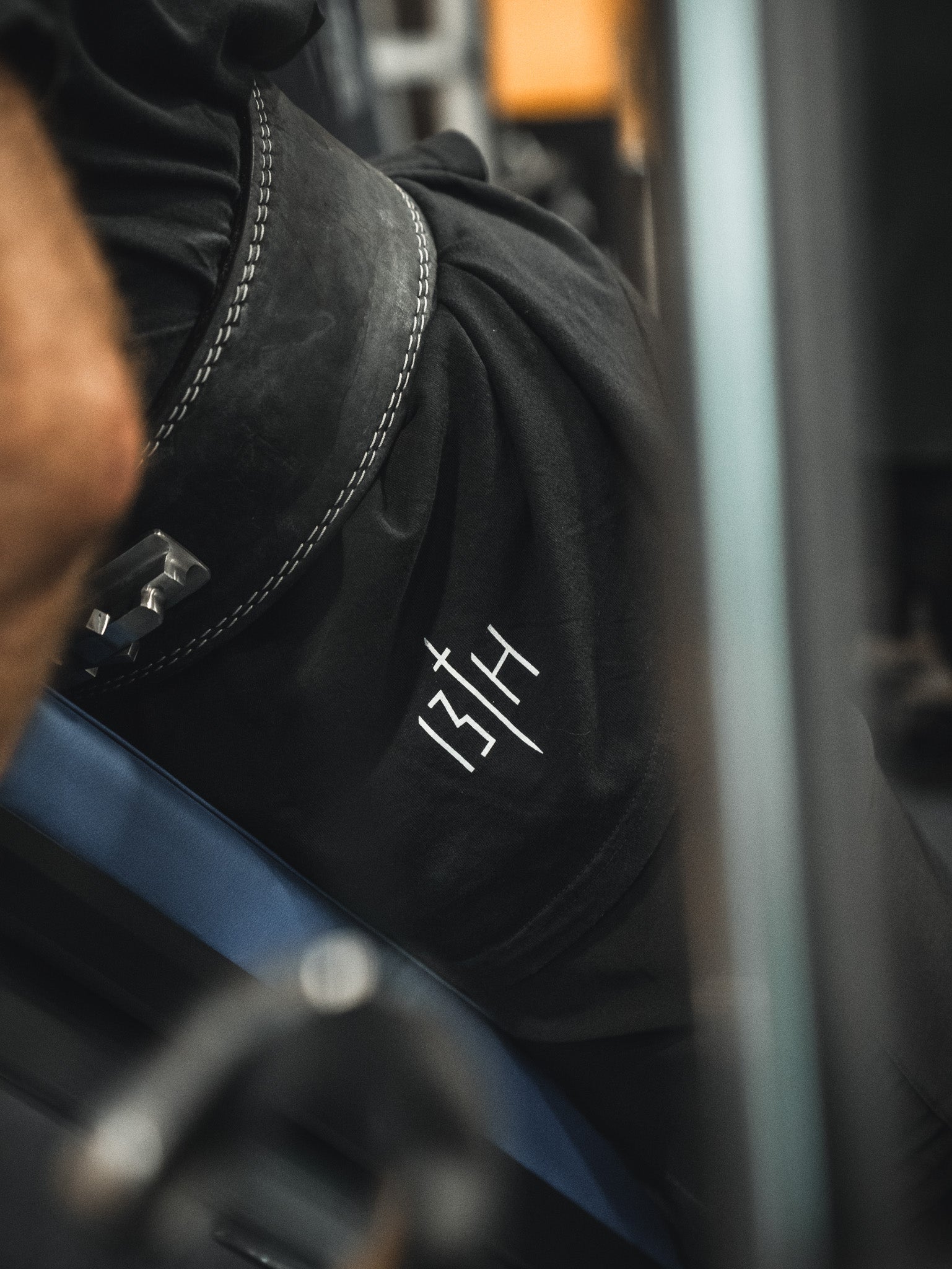 Close-up of a person in black 13th shorts and a weightlifting belt, wearing the Samson Premium Tee by 13th—faith-inspired athletic apparel—seated on gym equipment, preparing to lift.
