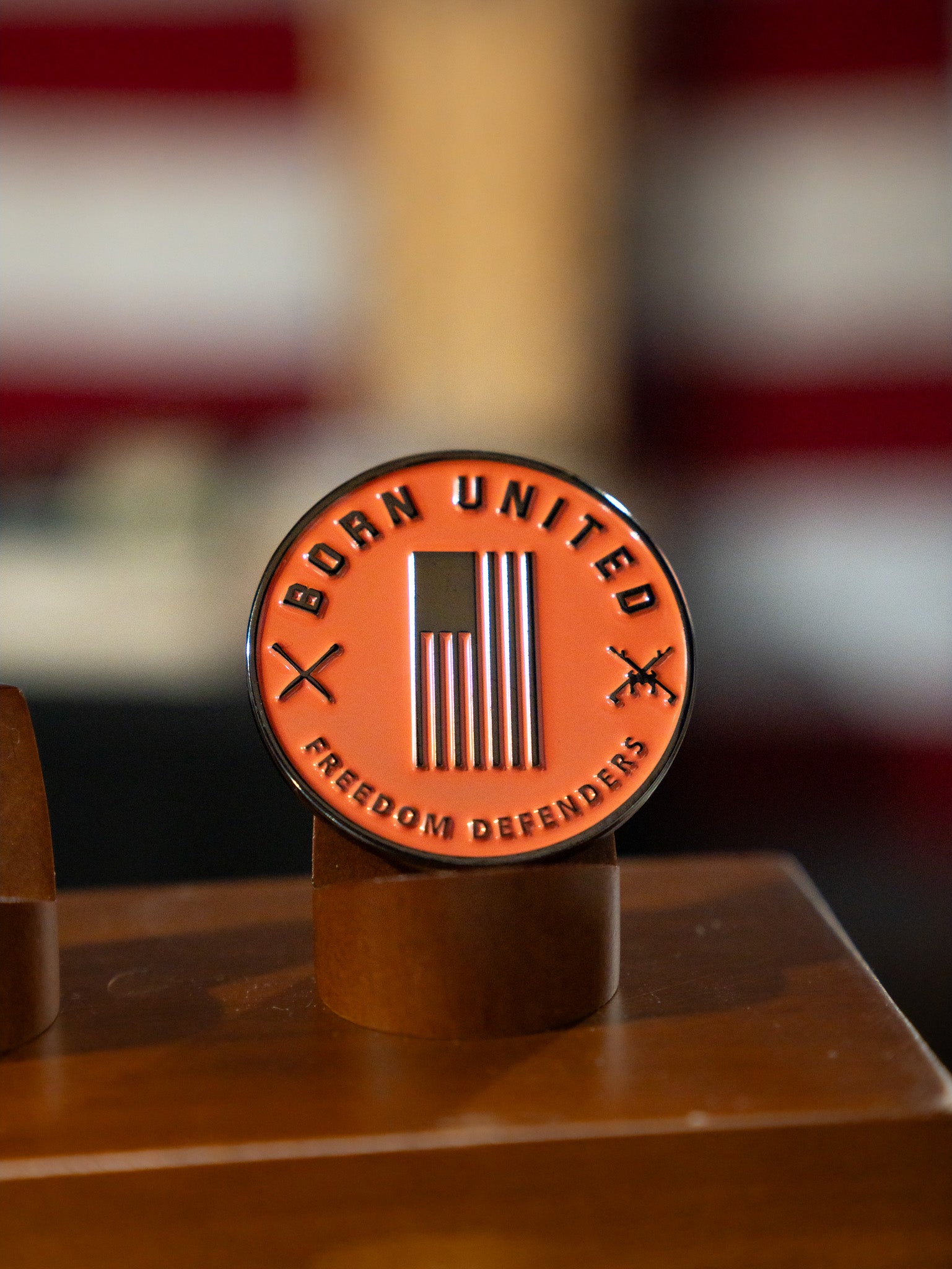 The Born United Private Label "Always Deadly Challenge Coin" features an American flag, “BORN UNITED” on top, “FREEDOM DEFENDERS” below, two crossed rifles, and the phrase Always Deadly. Displayed on a wooden stand.