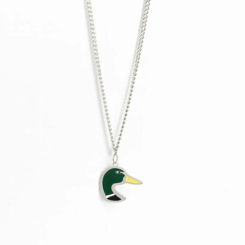 The Mucker Bucket Mallard OG necklace features a ducks head pendant with green and yellow enamel on a silver background, hanging elegantly from a stainless steel chain. Crafted in the USA, it combines quality artistry and craftsmanship.
