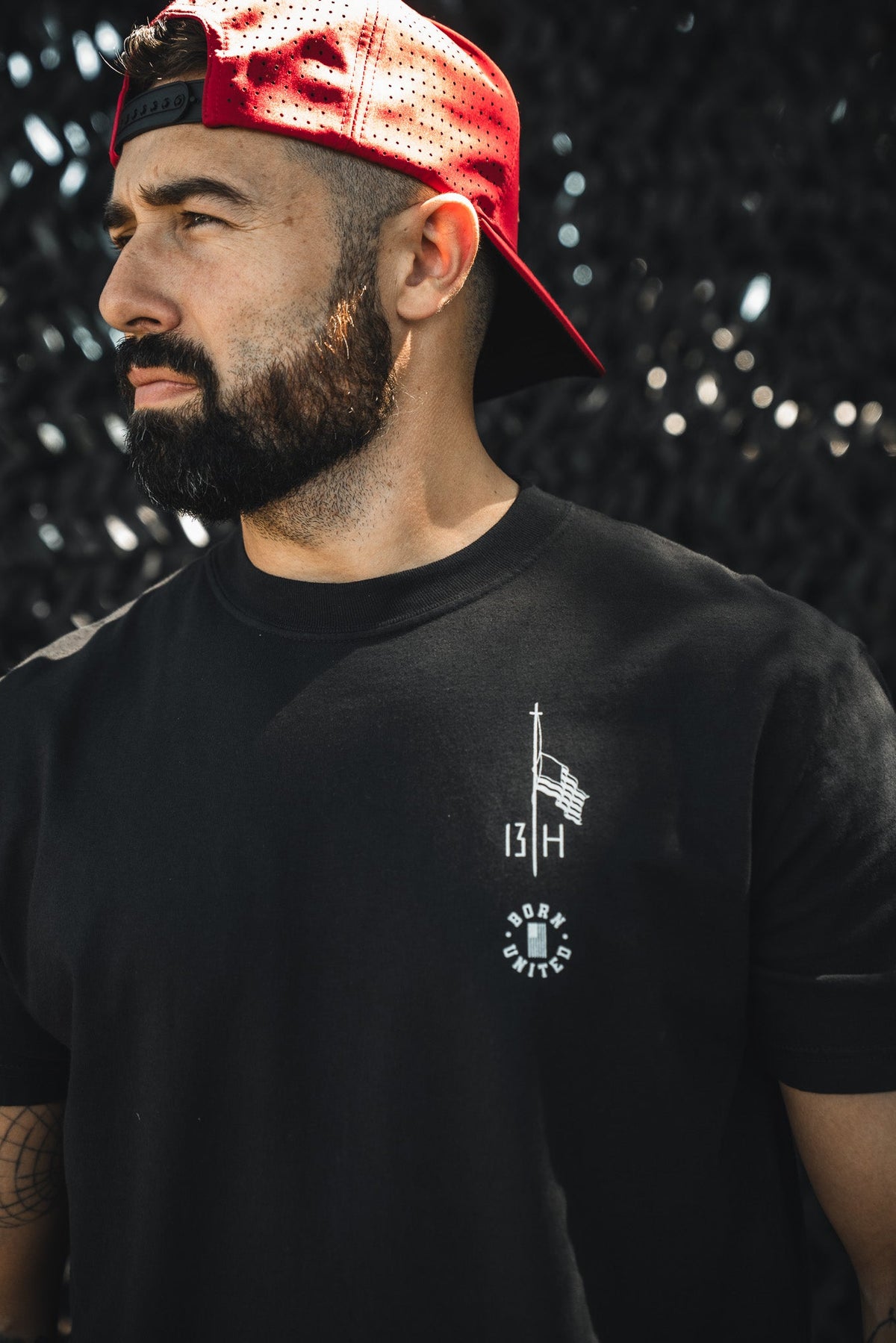 A bearded man in a backward red cap and a Born United Private Label "Live Like Charlie" tee stands before a dark textured background, gazing to the side.