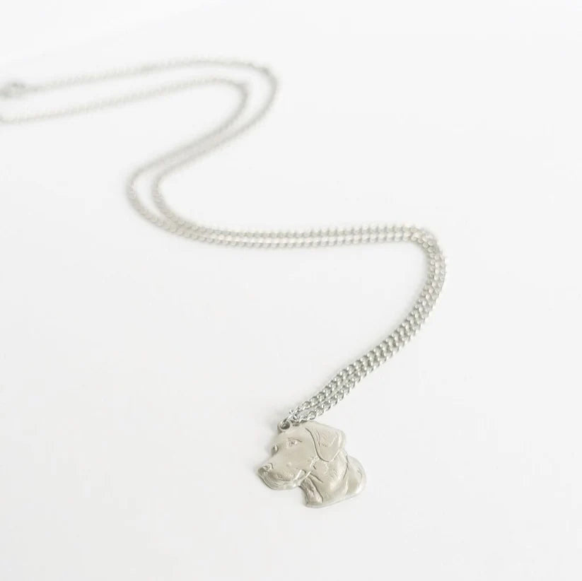 The Good Ol Boy- Stainless Steel Necklace by Mucker Bucket, featuring a silver pendant shaped like a dogs head with detailed engraving of its facial features and ears, rests on a white surface attached to a simple chain.