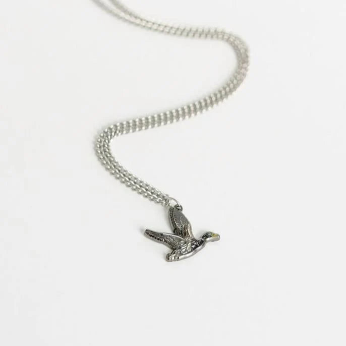 The Duck It OG Necklace by Mucker Bucket is a silver piece with a stainless steel pendant shaped like a flying bird, elegantly displayed on a white background.