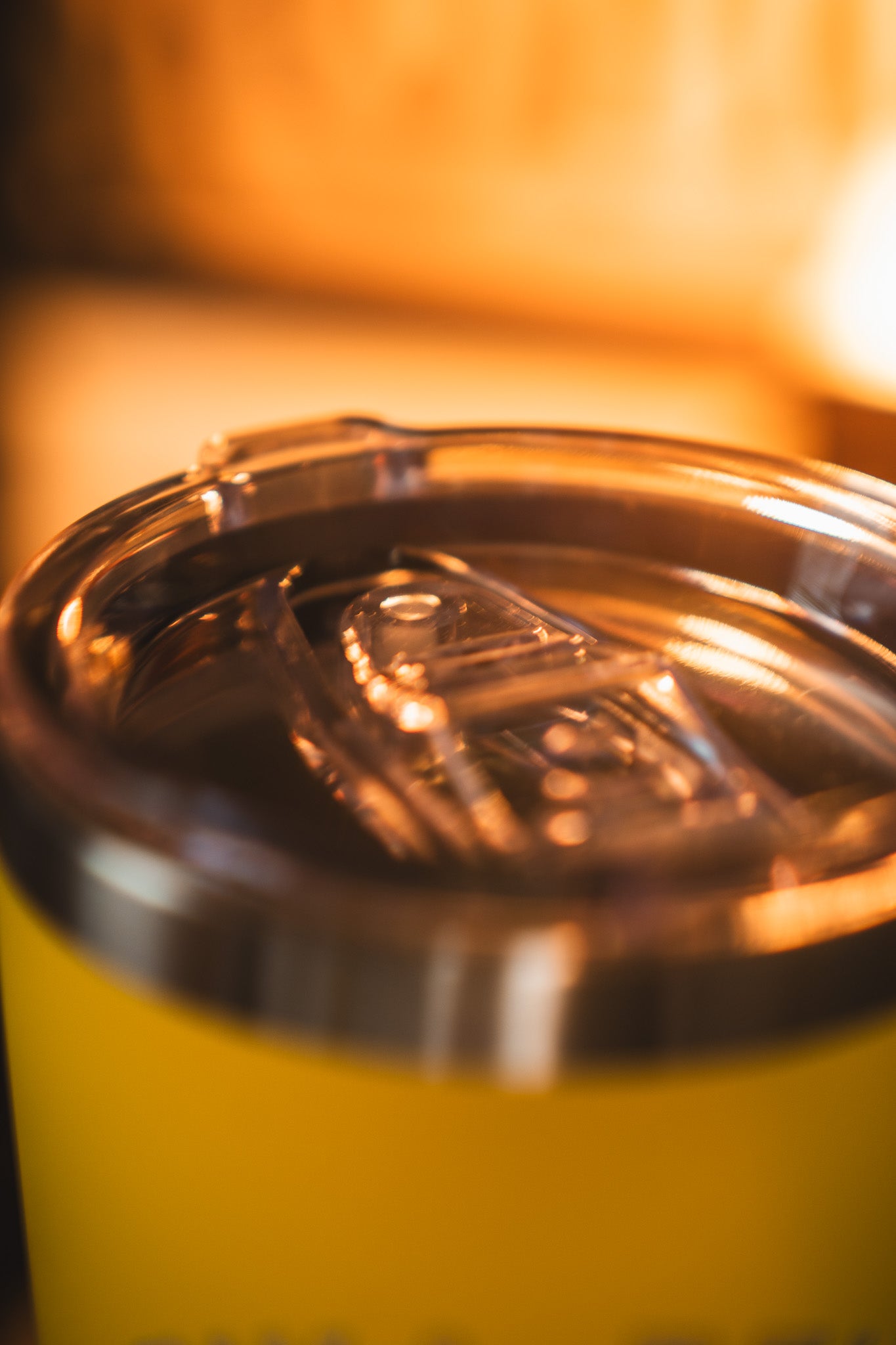 Close-up of the transparent plastic lid on the Born United Private Label Pika-Pew Tumbler - 20oz in yellow, with warm lighting adding a cozy feel in the background.