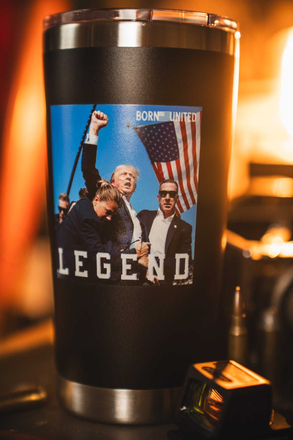 The Forever Legend Tumbler - 20oz from Born United Private Label is black and features a sticker with a man raising his fist among suited figures, an American flag backdrop, and the words BORN UNITED and LEGEND.