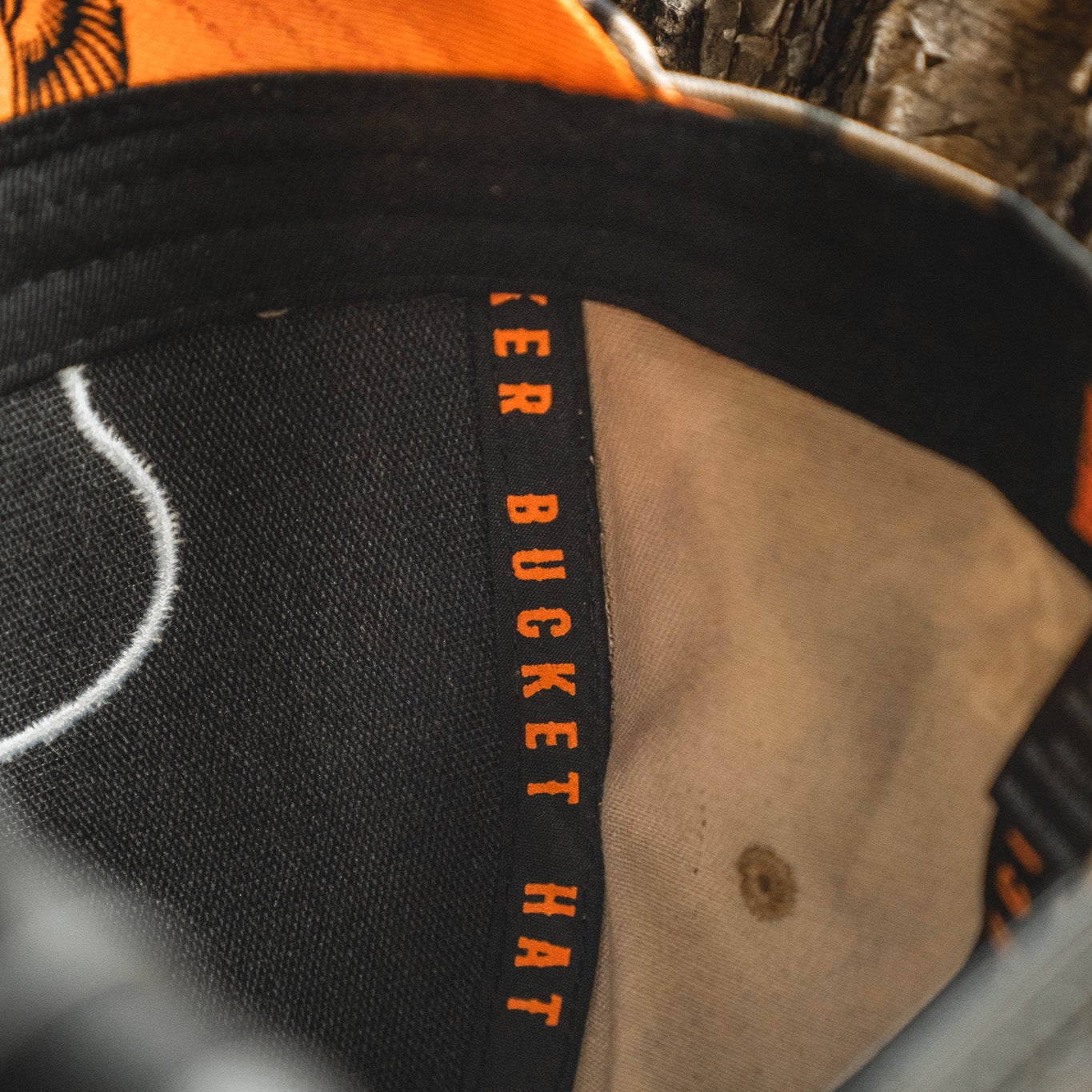 Close-up of the inside of the My Store Mallard Life Deadwood Camo Bucket hat, featuring orange "BUCKET HAT" text on the inner band and a worn, textured camo fabric inspired by mallard life.