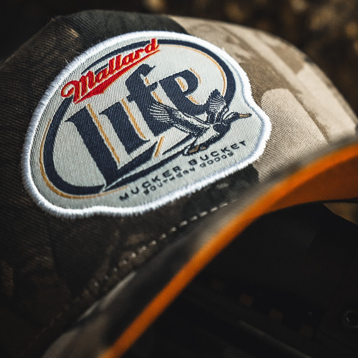 Close-up of the My Store Mallard Life Deadwood Camo Bucket, showing a patch with a flying duck and "Mallard Life" text prominently on the front.